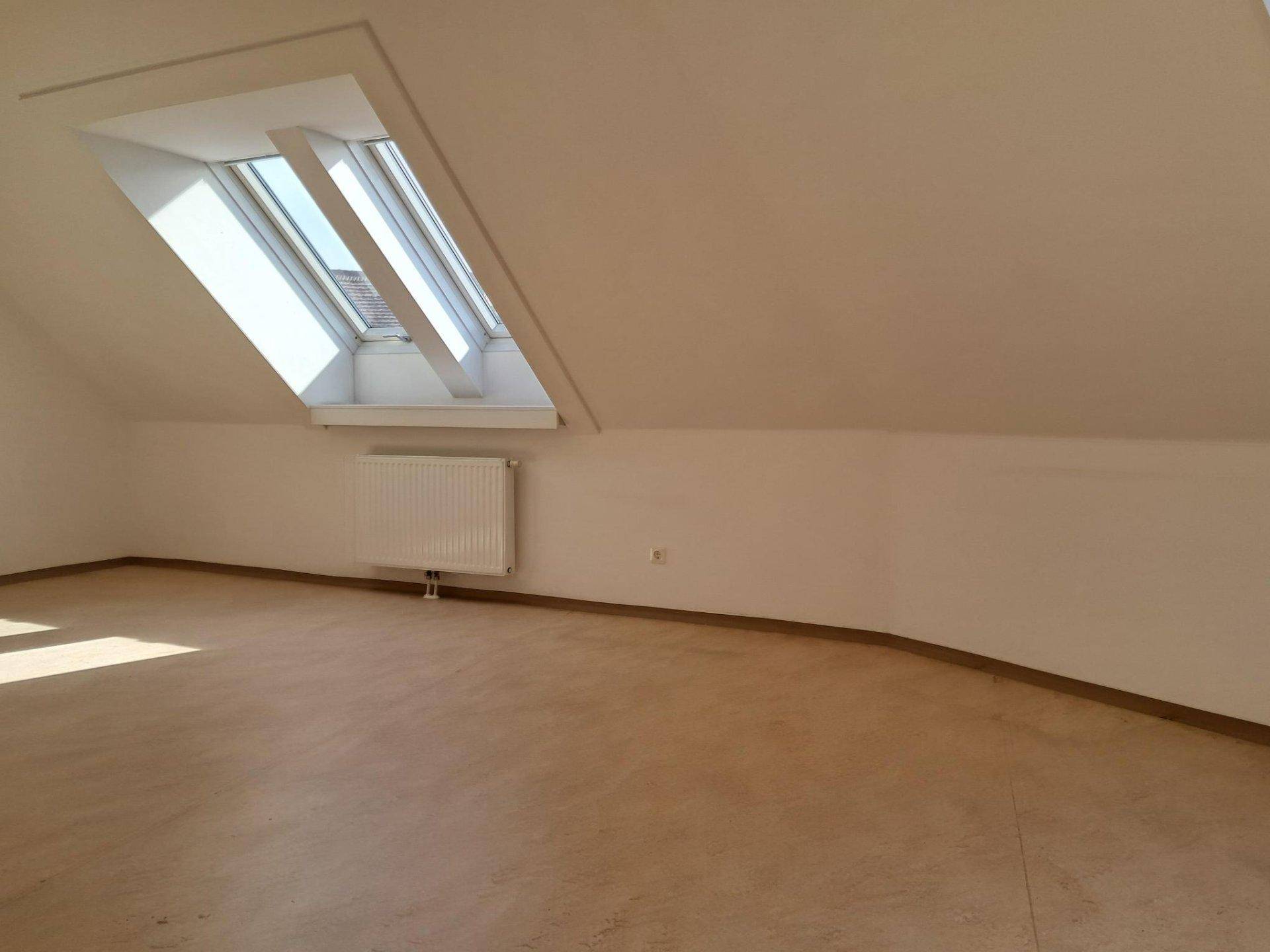 Heller Wohnraum im Dachgeschoss mit schrägen Wänden, Dachfenstern und hellem Laminatboden.