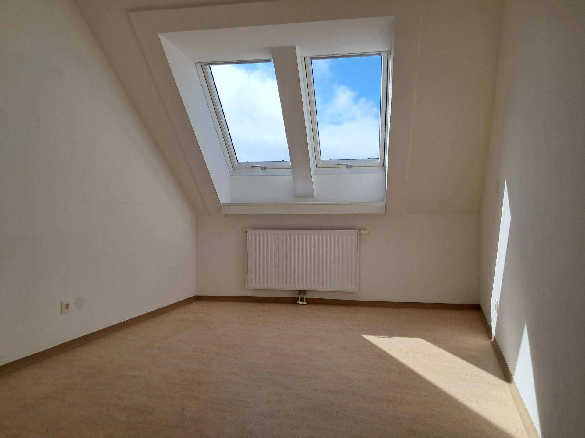 Helles Schlafzimmer im Dachgeschoss mit schrägen Wänden, großen Dachfenstern und Laminatboden.