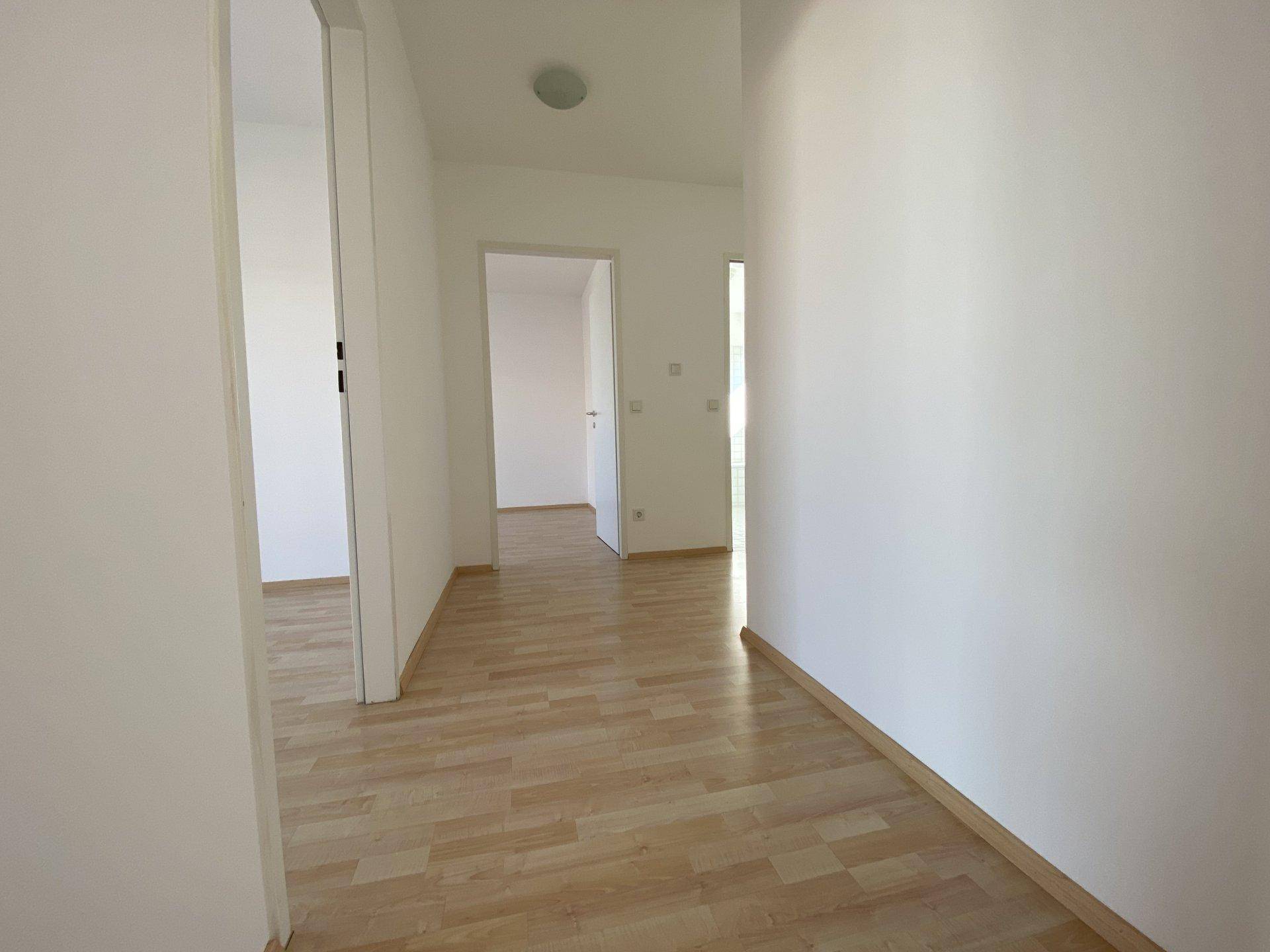 Langer, heller Flur mit Laminatboden, der zu verschiedenen Zimmern führt.