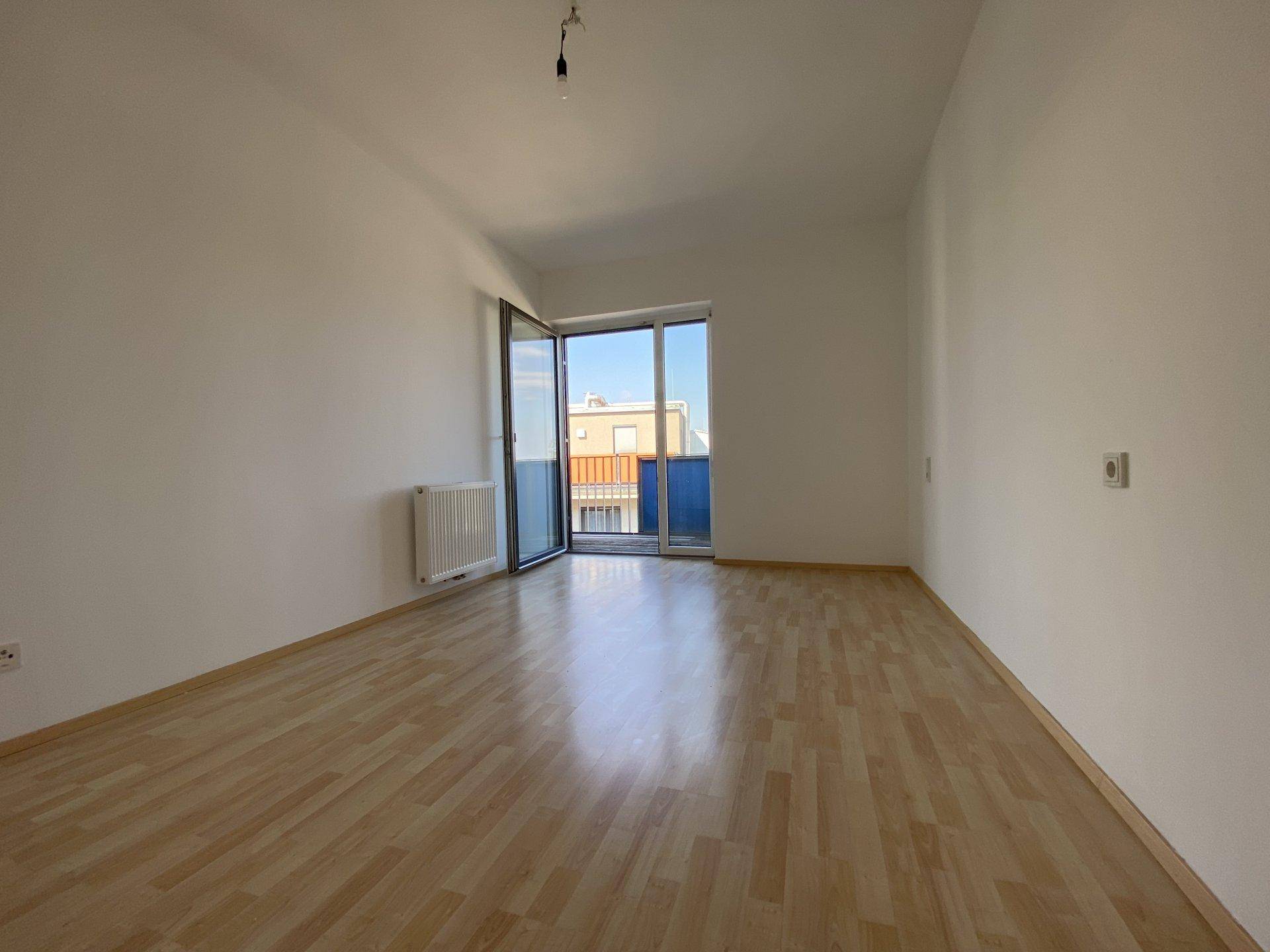 Geräumiges Wohnzimmer mit Laminatboden, Heizkörper und Zugang zu einem Balkon.