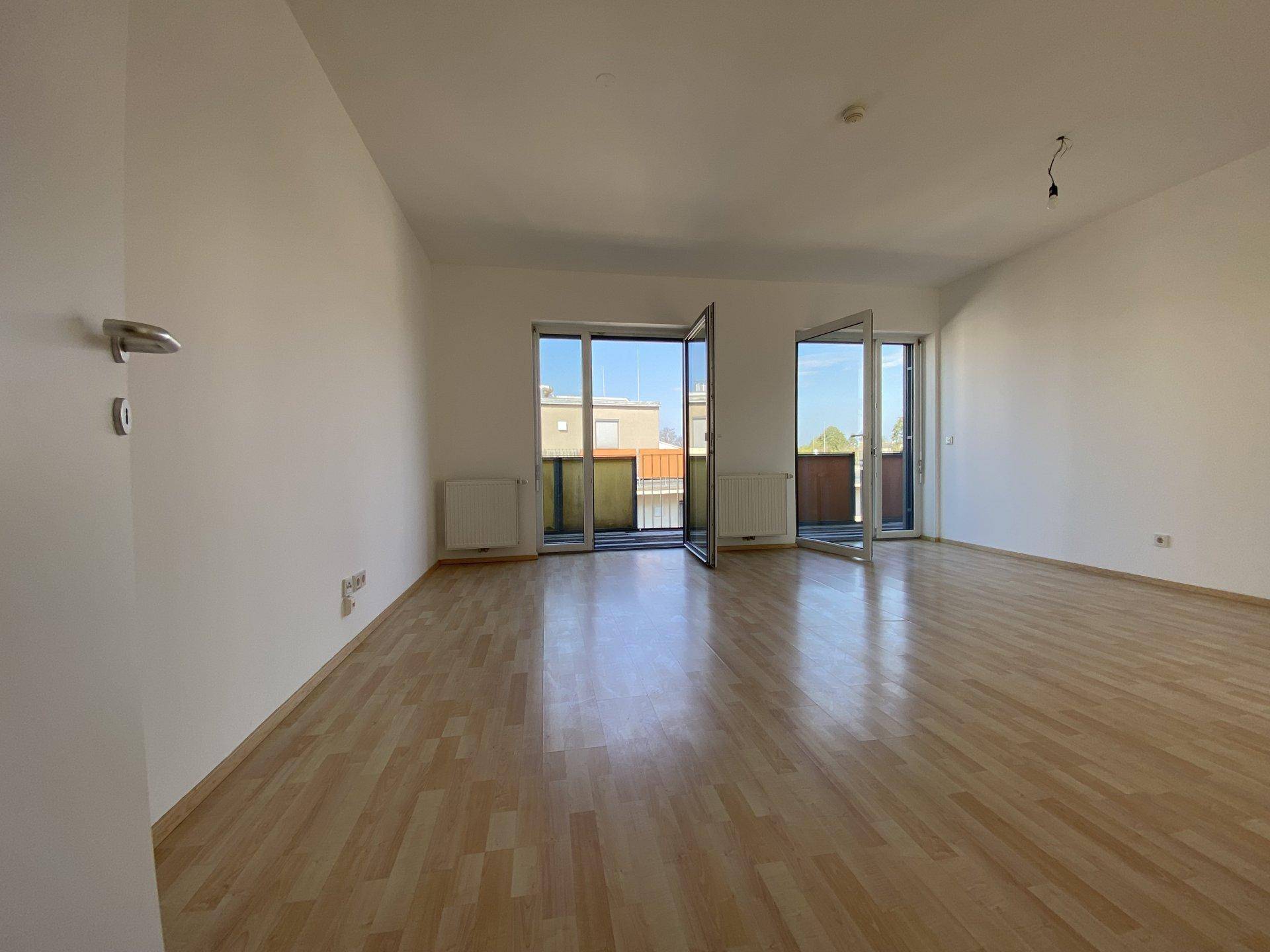 Helles Wohnzimmer mit Laminatboden und zwei Zugängen zu Balkonen.