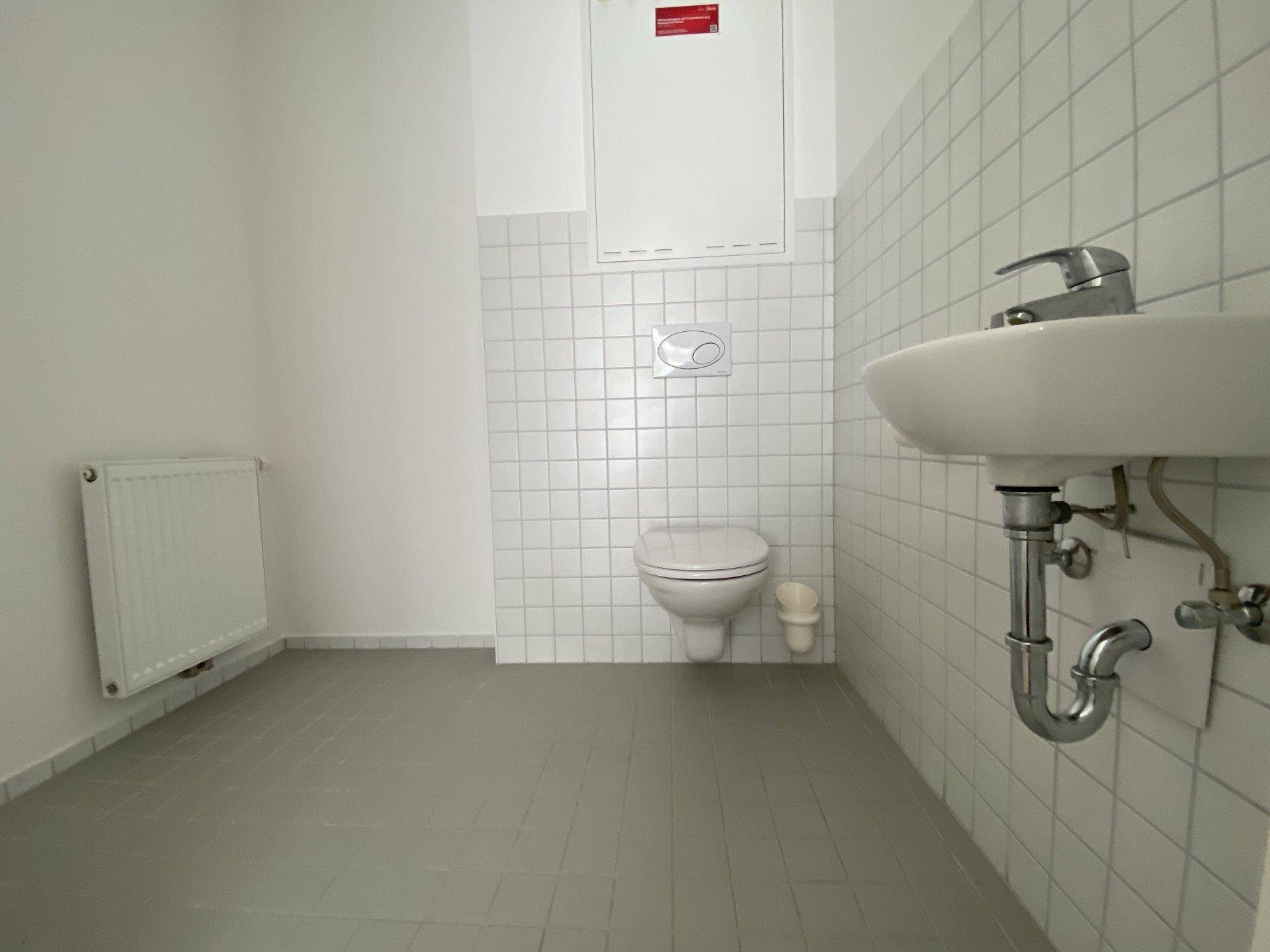 Separates WC mit wandhängender Toilette, Waschbecken und Heizkörper.