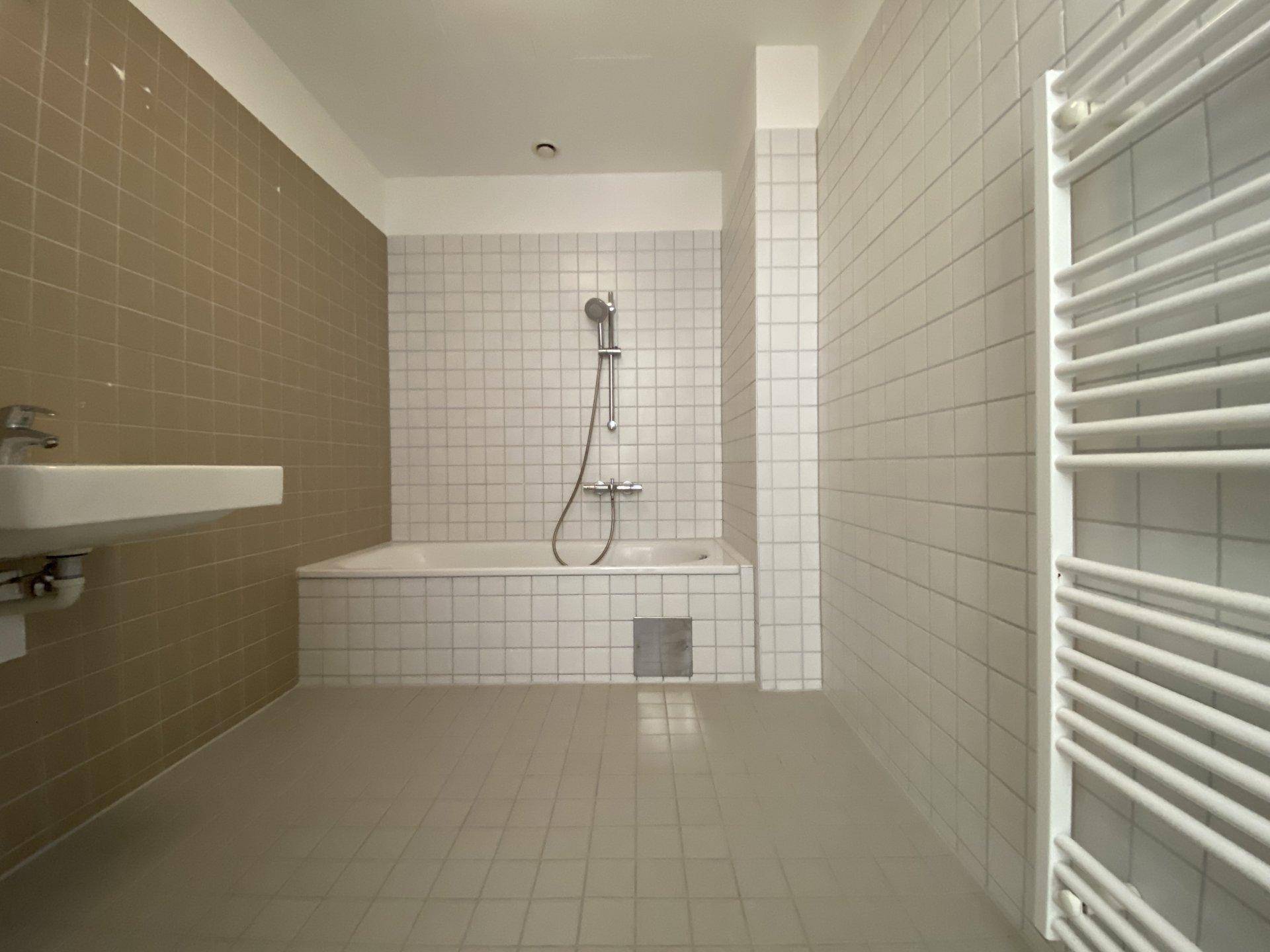 Badezimmer mit Badewanne, Duscharmatur, Waschbecken und beheiztem Handtuchhalter.