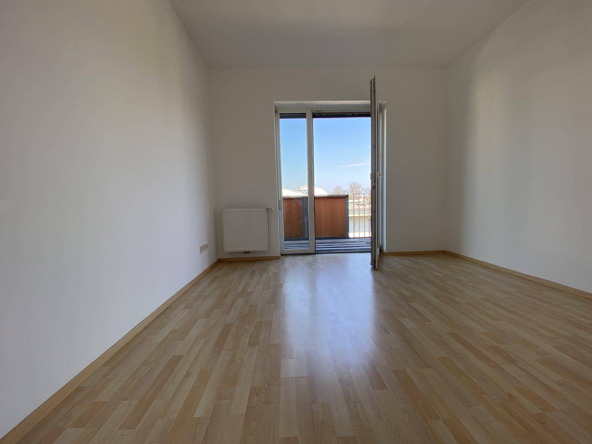 Geräumiges Schlafzimmer mit Laminatboden und großem Fenster mit Balkonzugang.