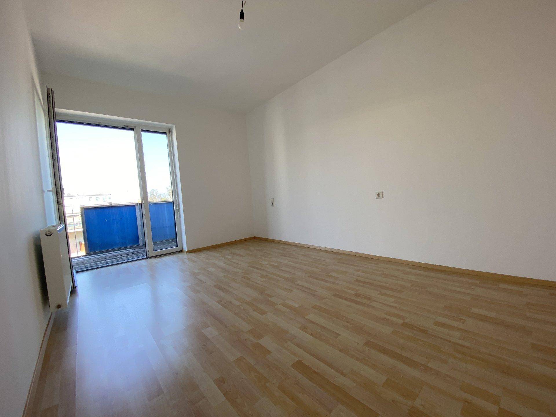 Helles Schlafzimmer mit Laminatboden, Heizkörper und Zugang zu einem Balkon.