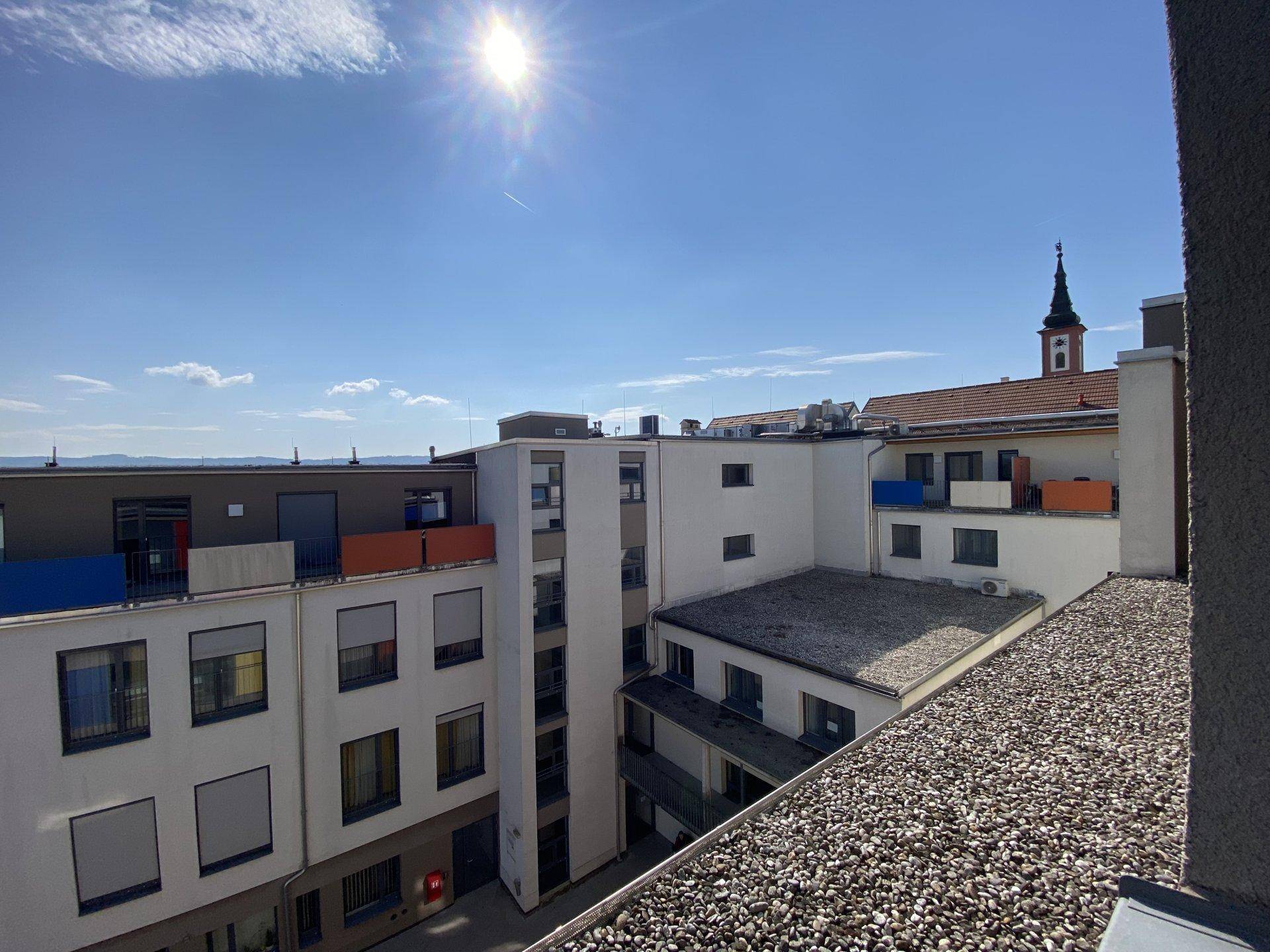 Dachansicht der Wohnanlage mit Blick auf umliegende Gebäude und einen Kirchturm in der Ferne.