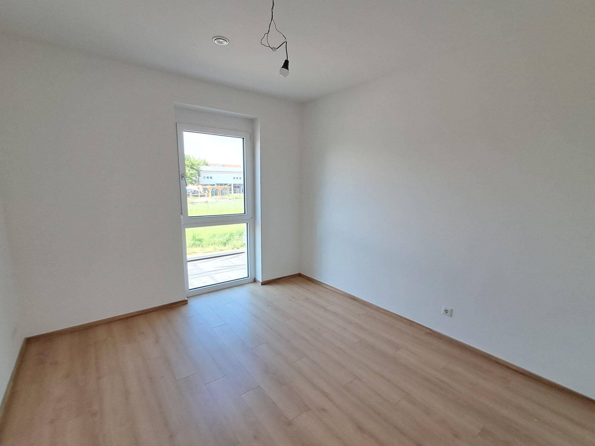 Helles Schlafzimmer mit Laminatboden und Fenster mit Blick ins Grüne.