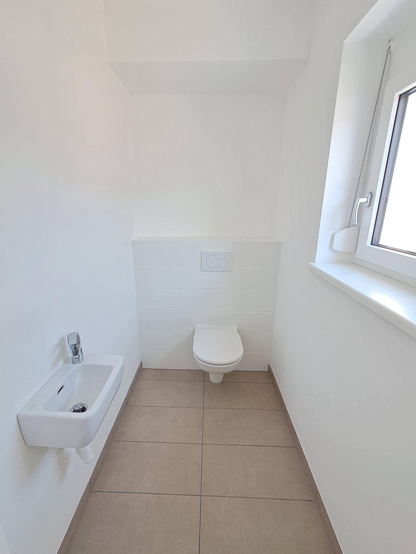 Modernes Gäste-WC mit wandhängendem WC, kleinem Waschbecken und Fenster.