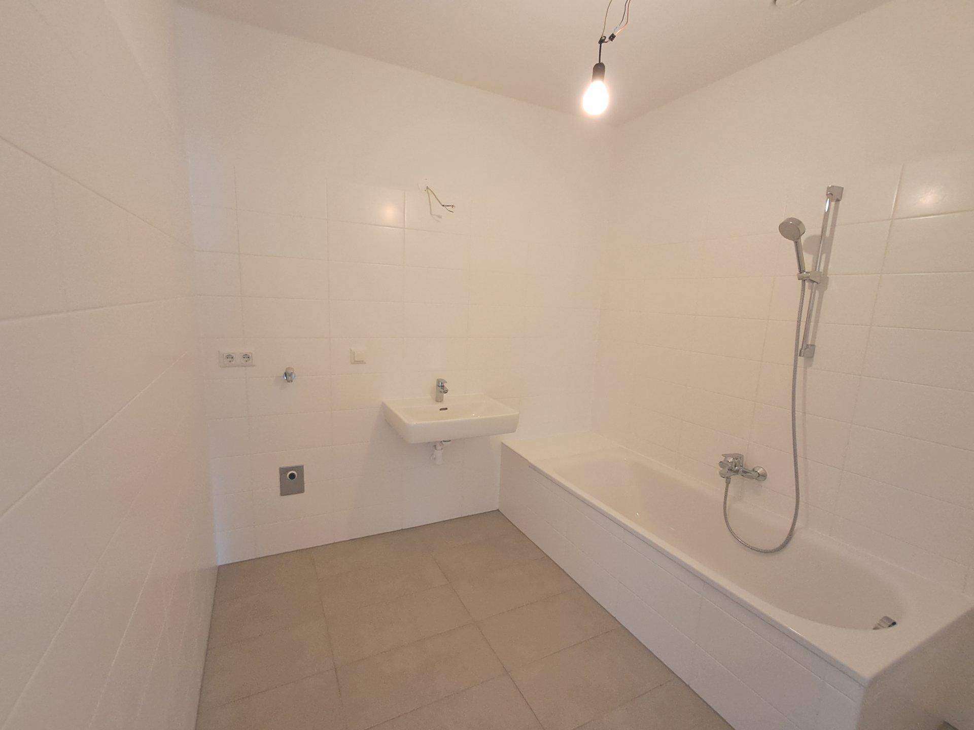 Modernes Badezimmer mit weißen Fliesen, einer Badewanne und einem Waschbecken, bereit zur Fertigstellung.
