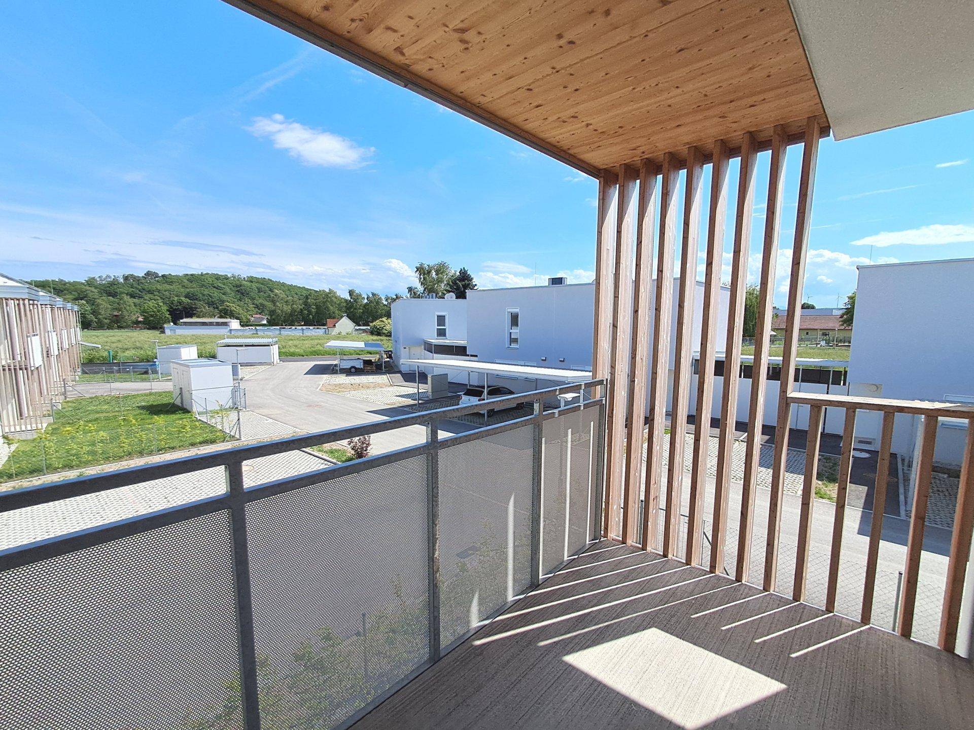 Geräumiger Balkon mit Holzverkleidung und Blick auf die umliegende Wohnsiedlung und Parkplätze.