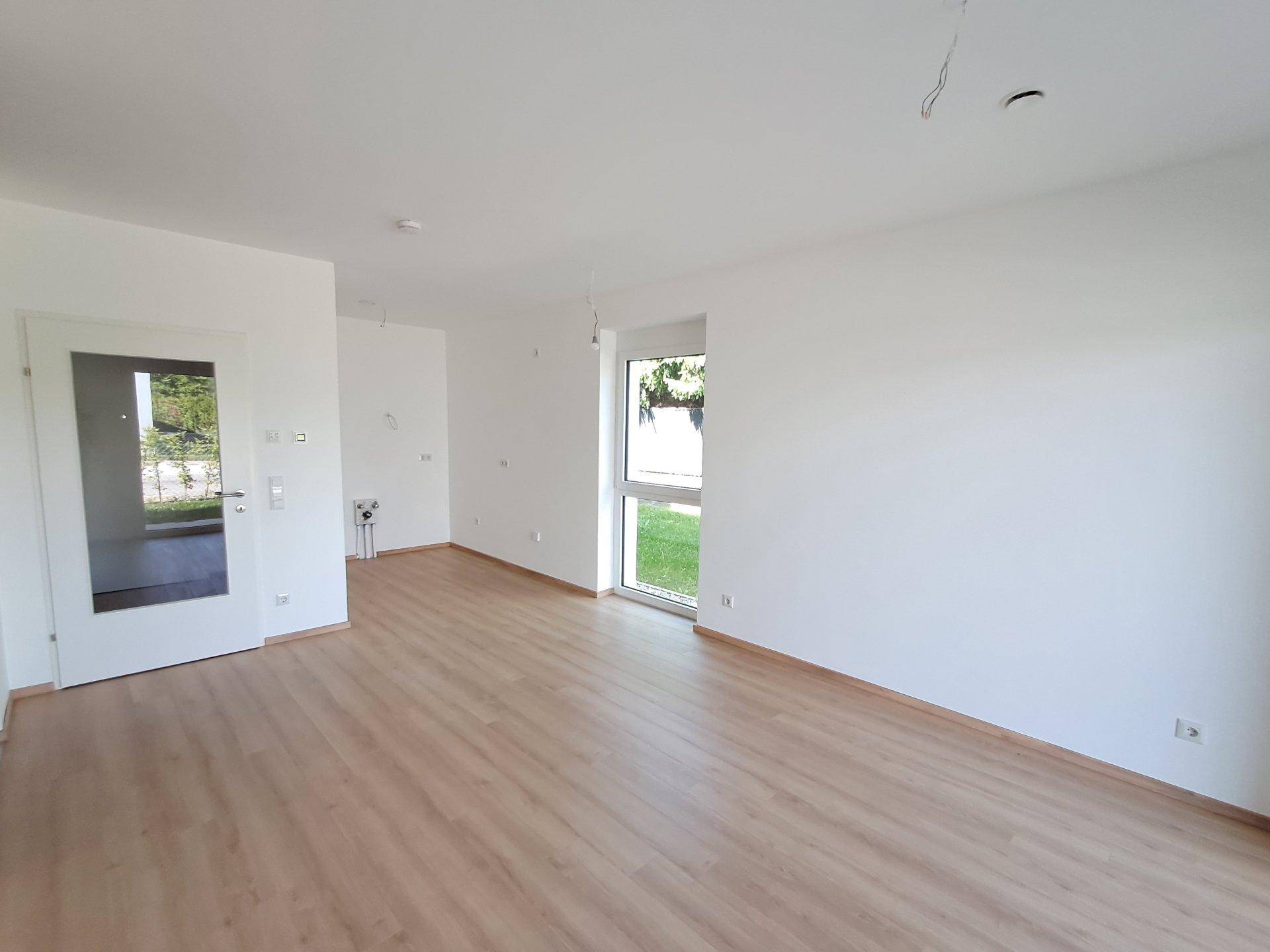 Geräumiger, heller Wohnbereich mit Laminatboden und viel Tageslicht durch große Fenster.