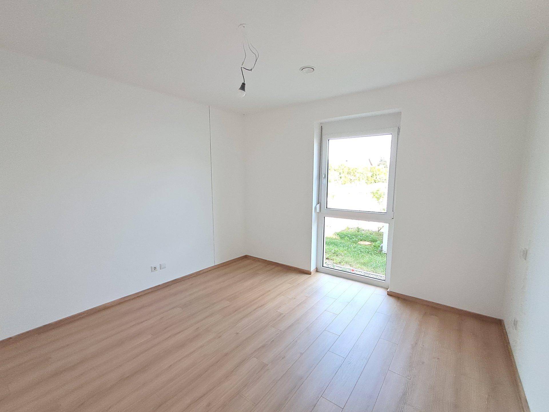 Helles Schlafzimmer mit Laminatboden und Fenster mit Blick ins Grüne.
