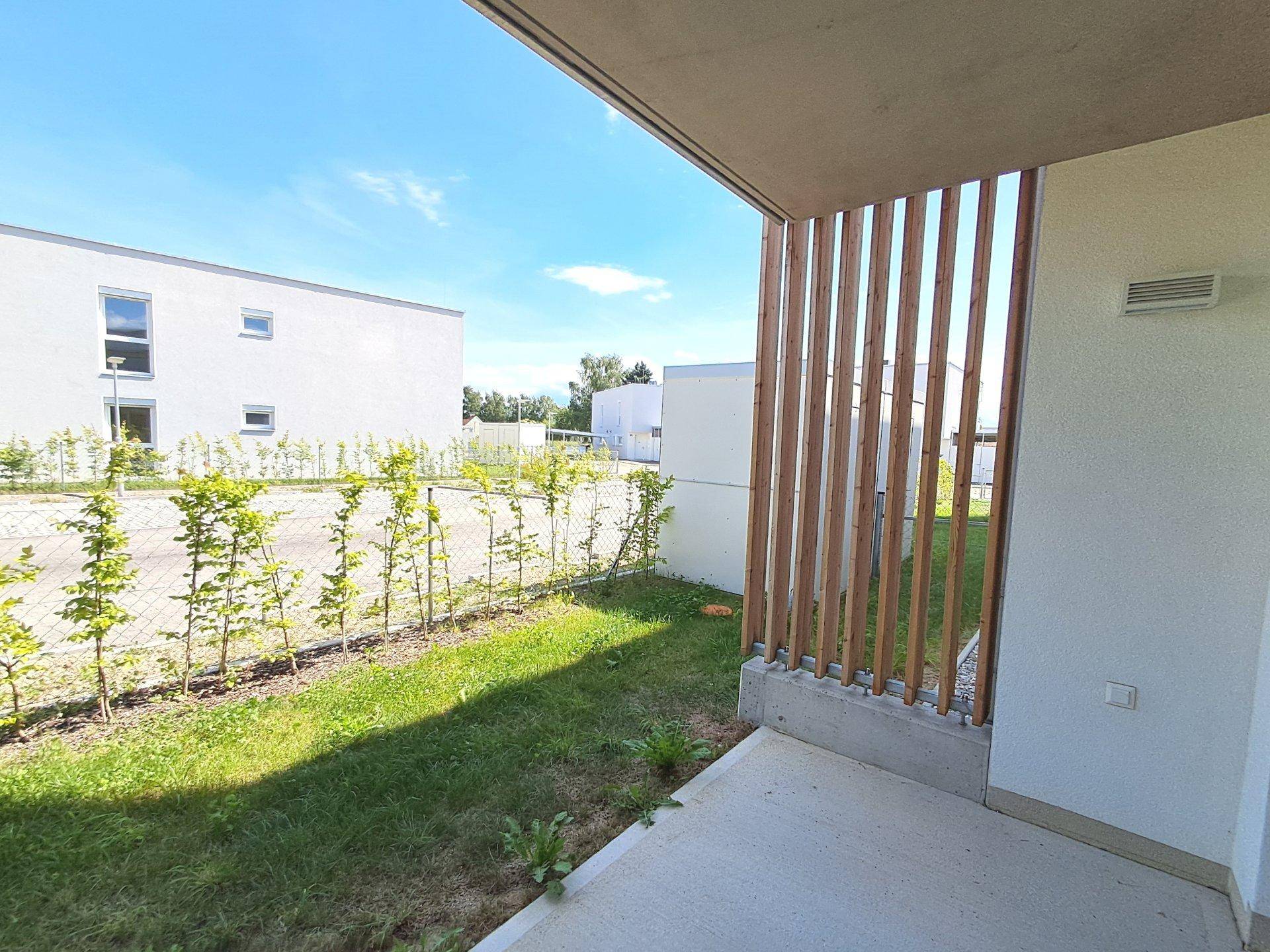 Kleine Terrasse mit Holzelementen und direktem Zugang zu einer grünen Rasenfläche.