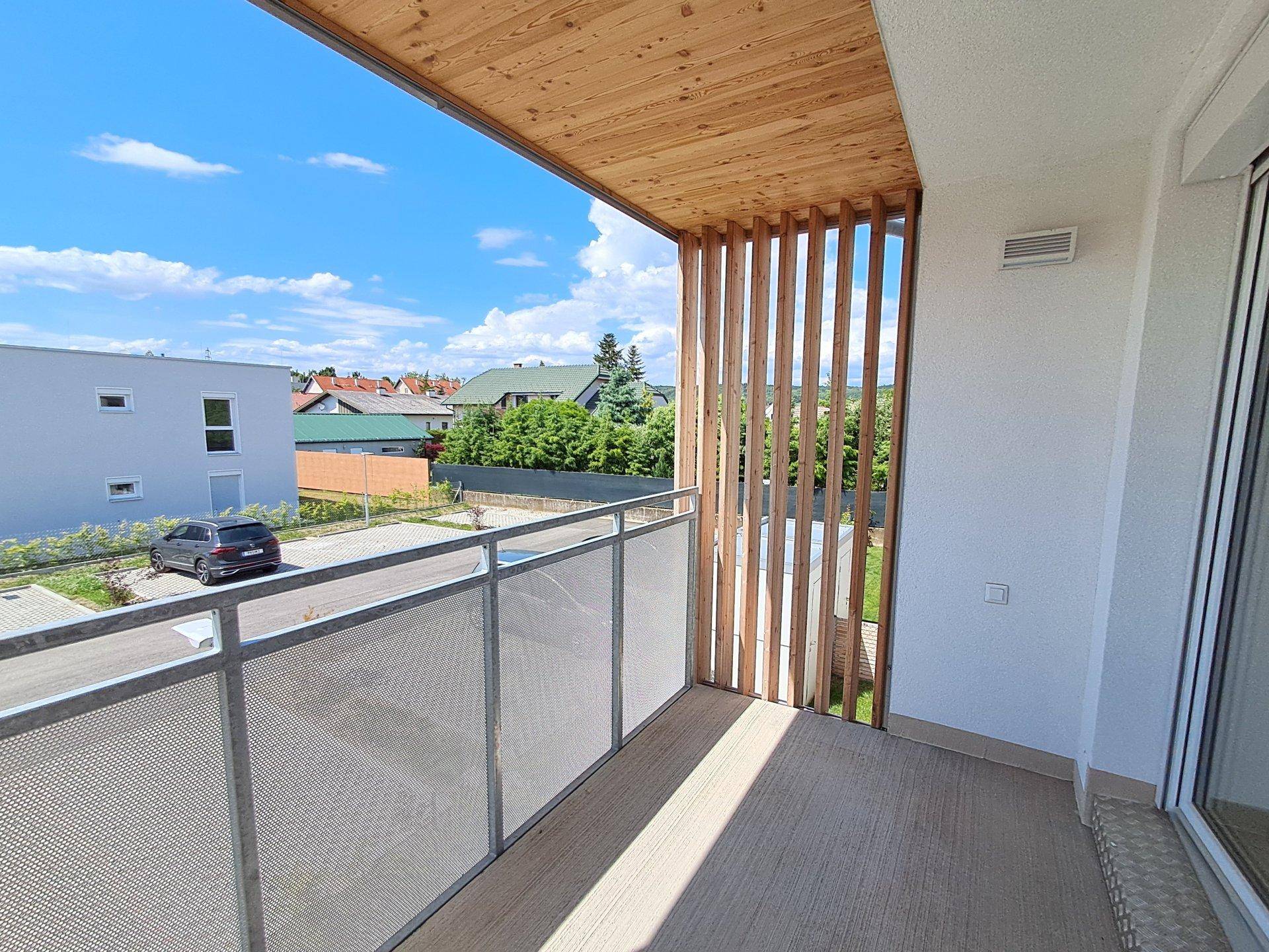 Heller Balkon mit Holzelementen und Metallgeländer, der einen weiten Blick über die Nachbarschaft bietet.
