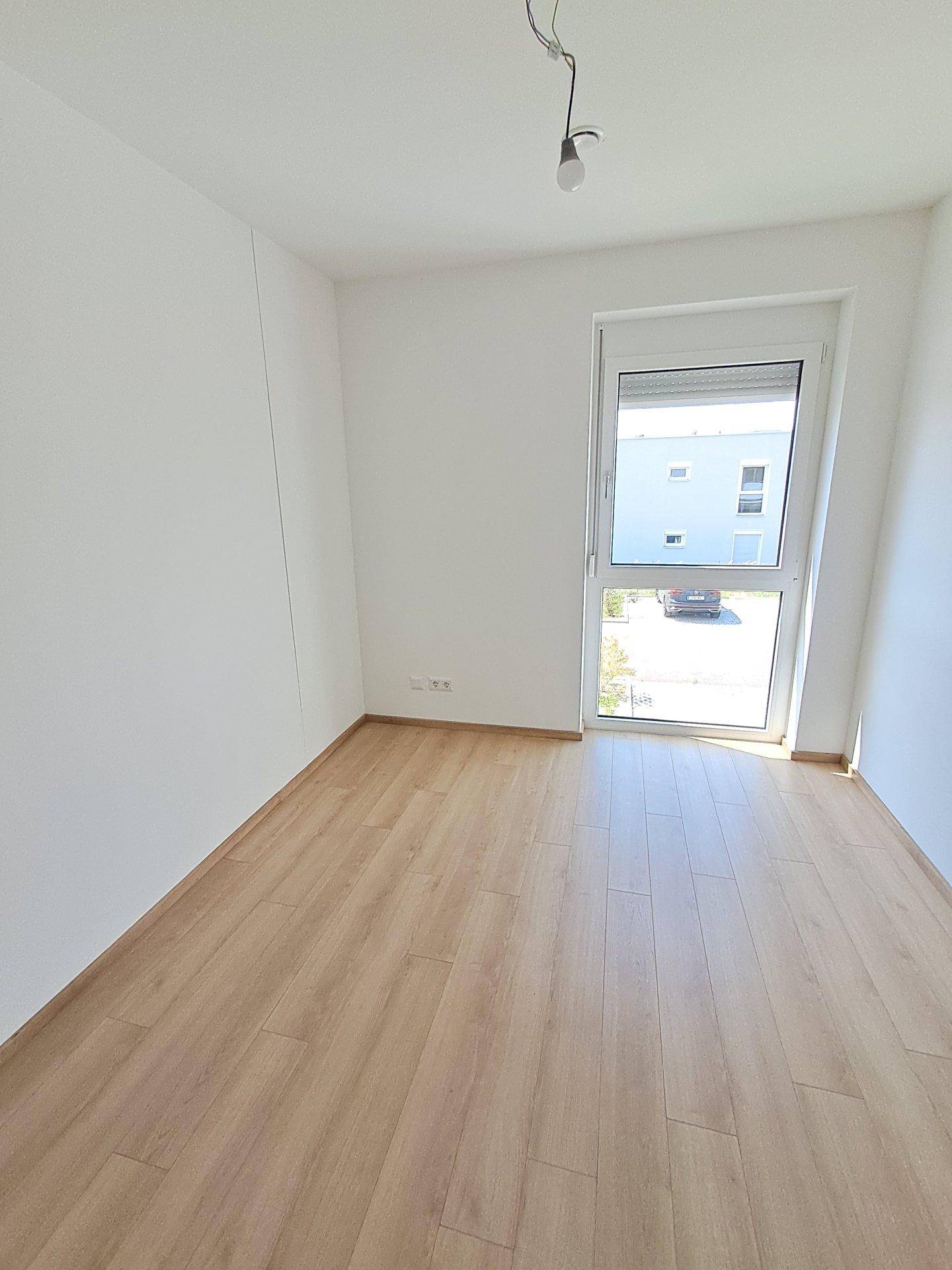 Helles Schlafzimmer mit Laminatboden, weißen Wänden und einem großen Fenster für viel Tageslicht.