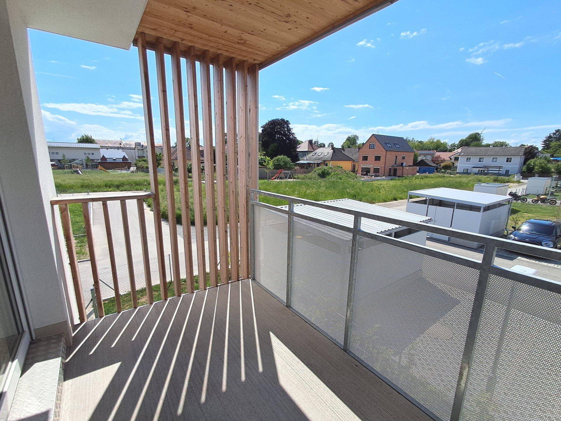 Balkon mit Holzelementen und Metallgeländer bietet Blick auf die Umgebung und weitere Häuser.