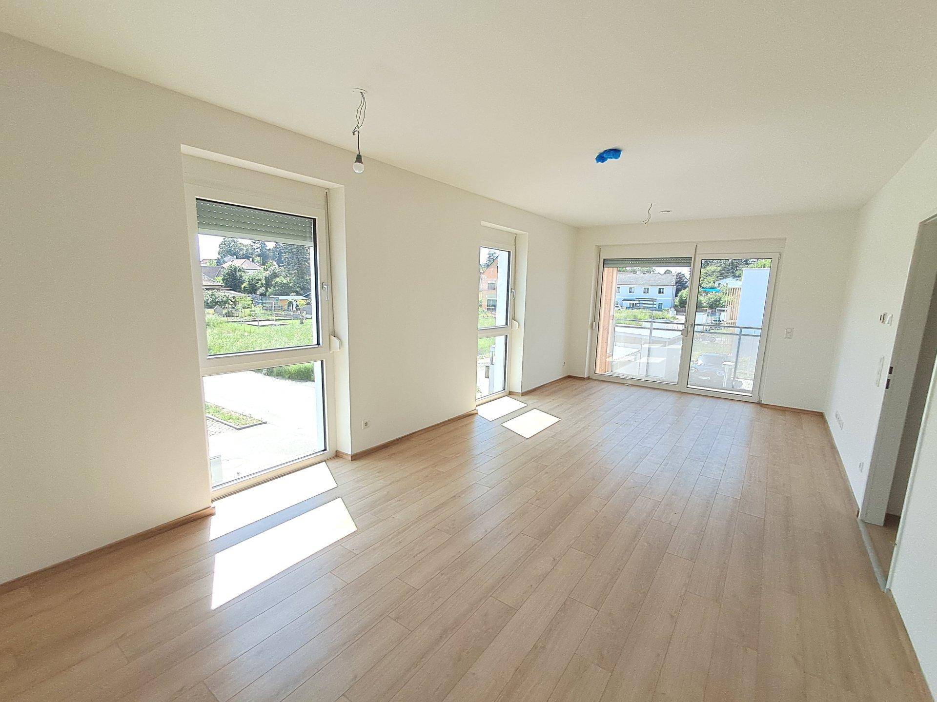 Helles Wohnzimmer mit Laminatboden, weißen Wänden und großen Fenstern mit Zugang zum Außenbereich.