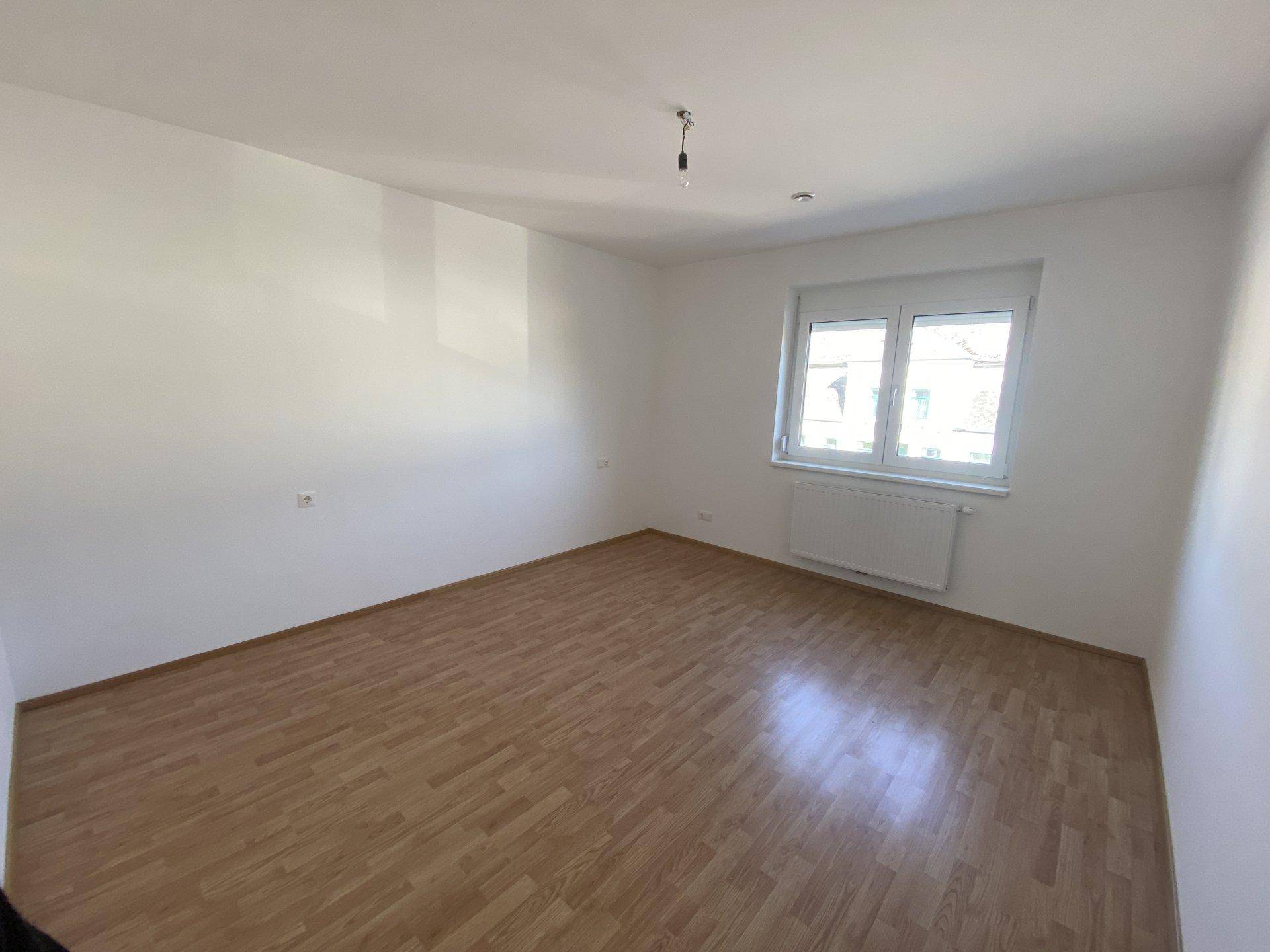 Geräumiges, helles Schlafzimmer mit Parkettboden und einem großen Fenster.