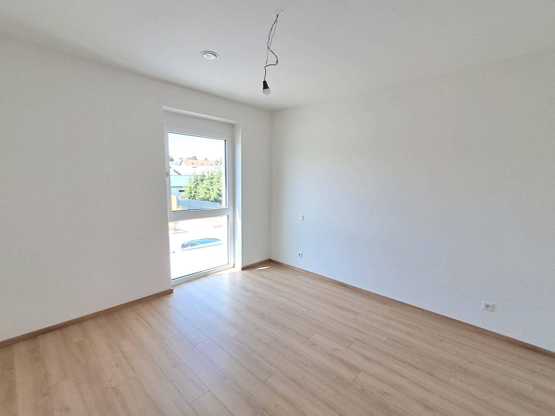 Geräumiges Schlafzimmer mit hellem Laminatboden und einem großen Fenster, das den Raum gut belichtet.