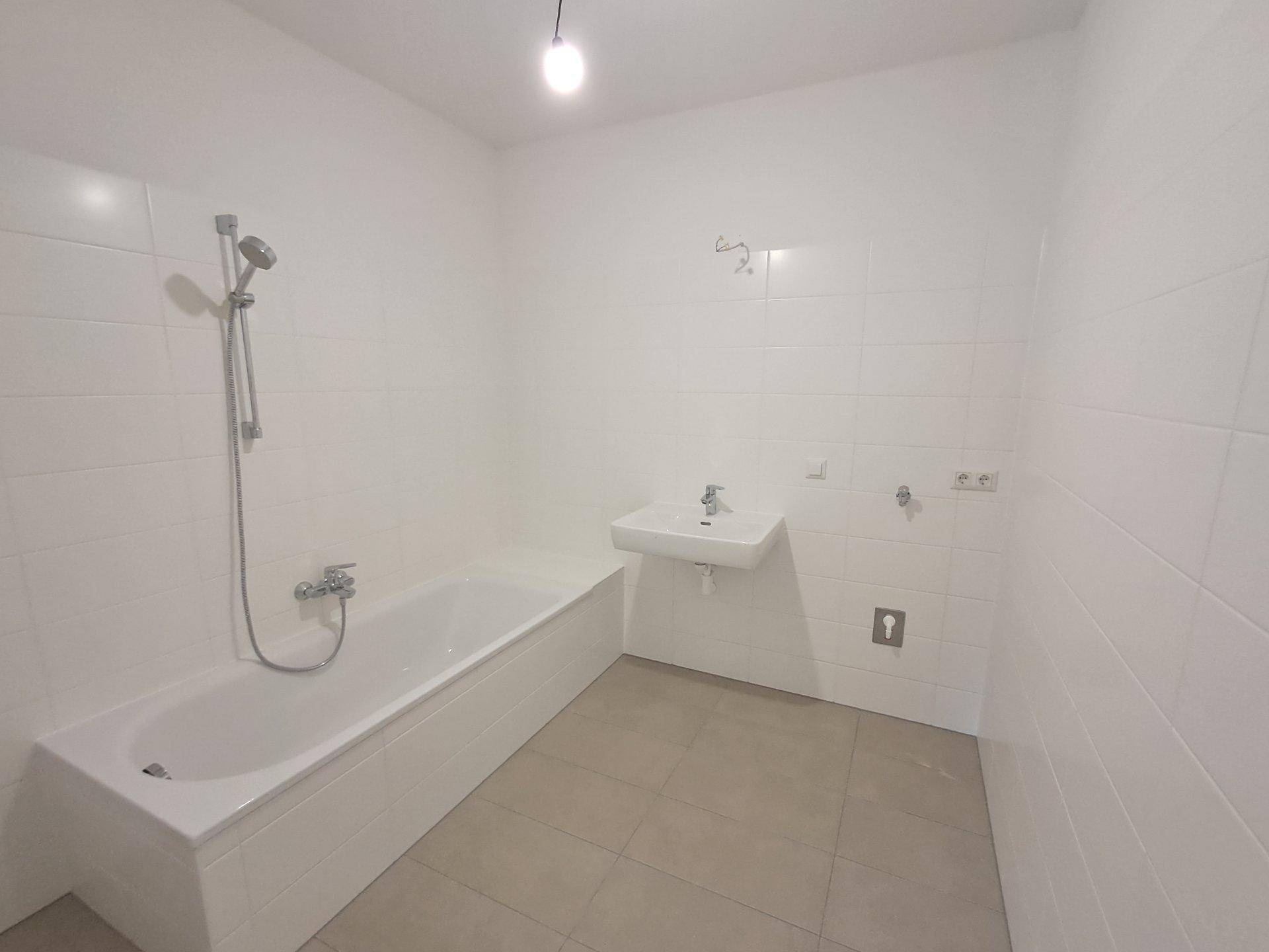 Modernes Badezimmer mit weißen Fliesen, Badewanne mit Duschfunktion und einem einzelnen Waschbecken.