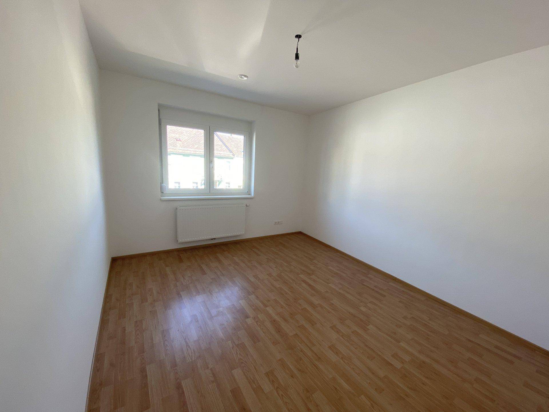Weiteres helles Schlafzimmer mit Parkettboden und Fenster, bereit zur Einrichtung.