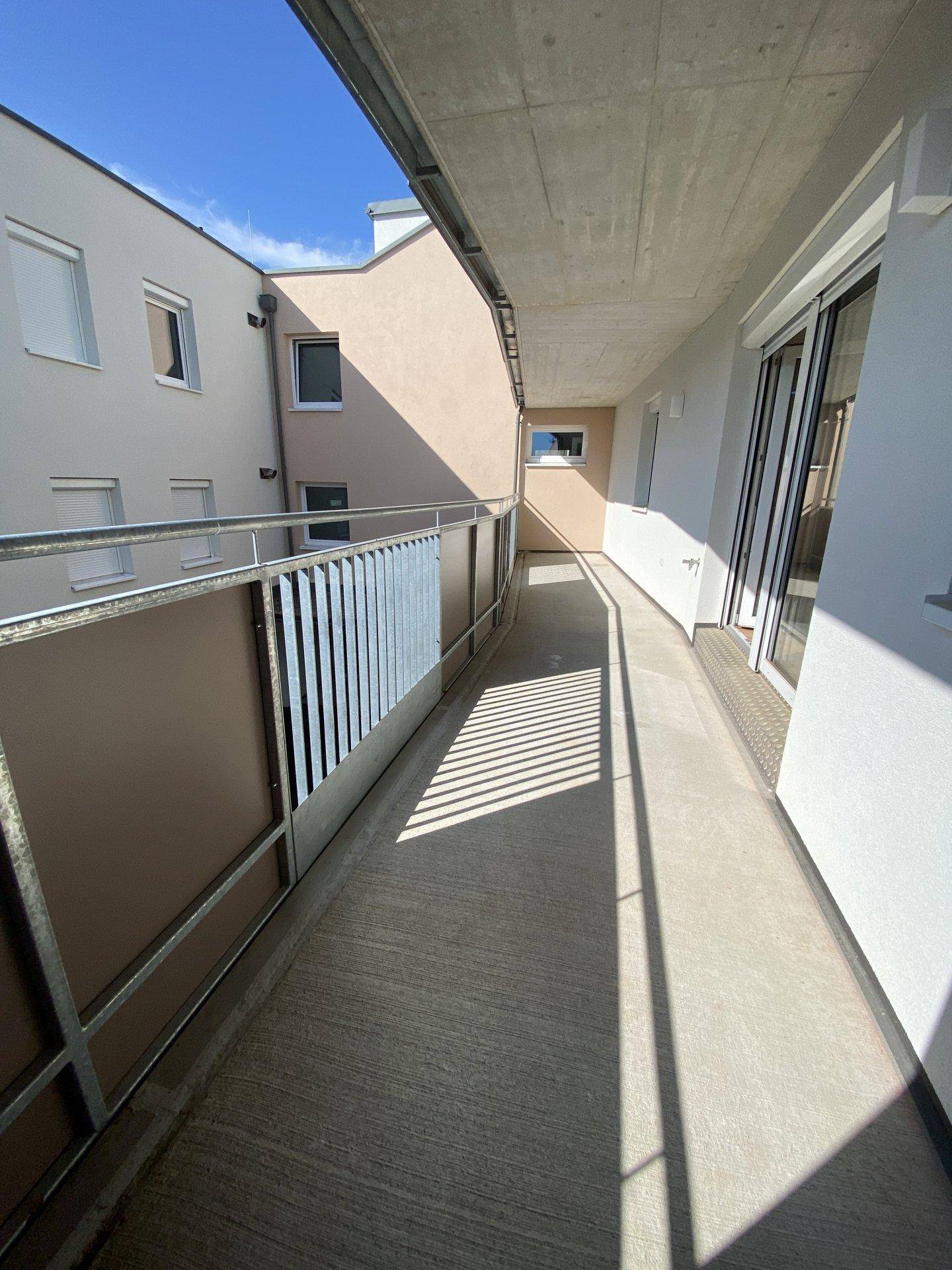 Langer, schmaler Balkon mit Metallgeländer und Blick auf den Innenhof der Wohnanlage.