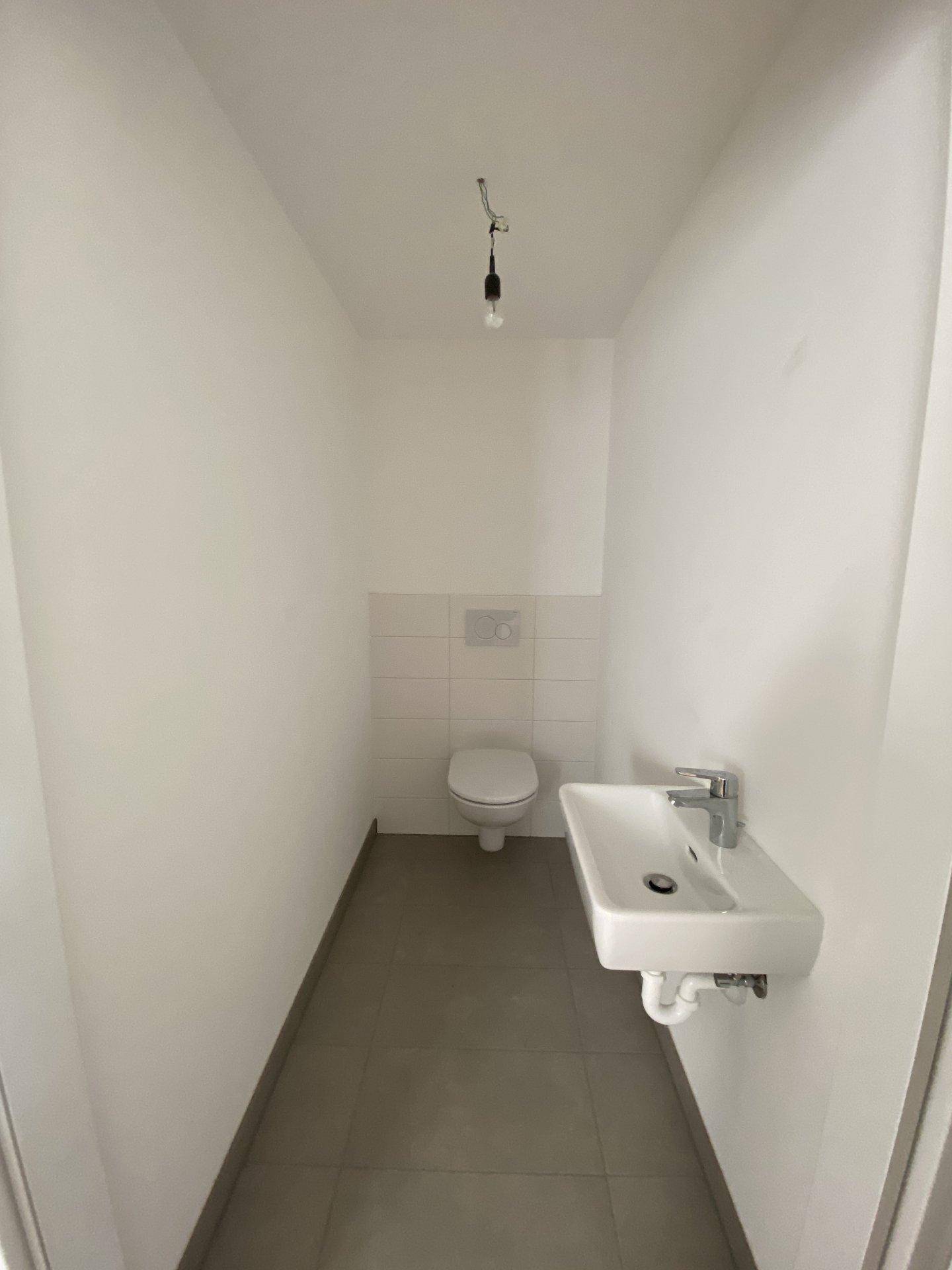 Separates Gäste-WC mit Wand-WC, kleinem Waschbecken und Fliesenboden.