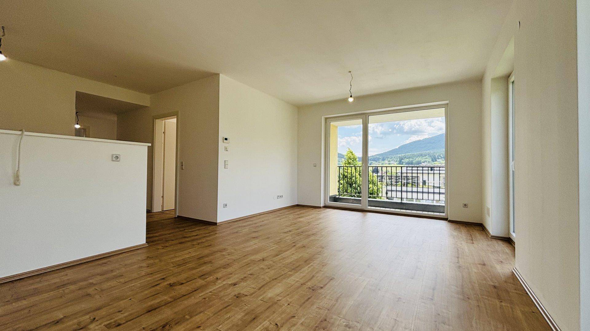 Heller Wohnbereich mit Laminatboden und Schiebetür zum Balkon mit Bergblick.