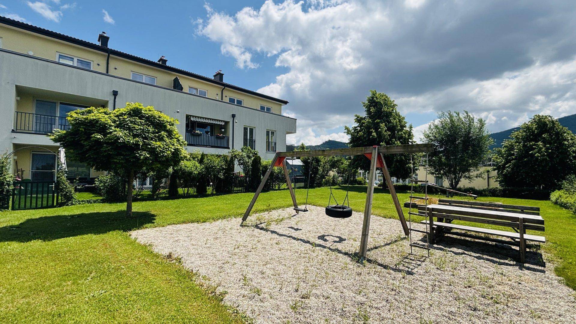 Kinderspielplatz mit Schaukeln und Sandfläche vor dem Wohngebäude mit Balkonen.