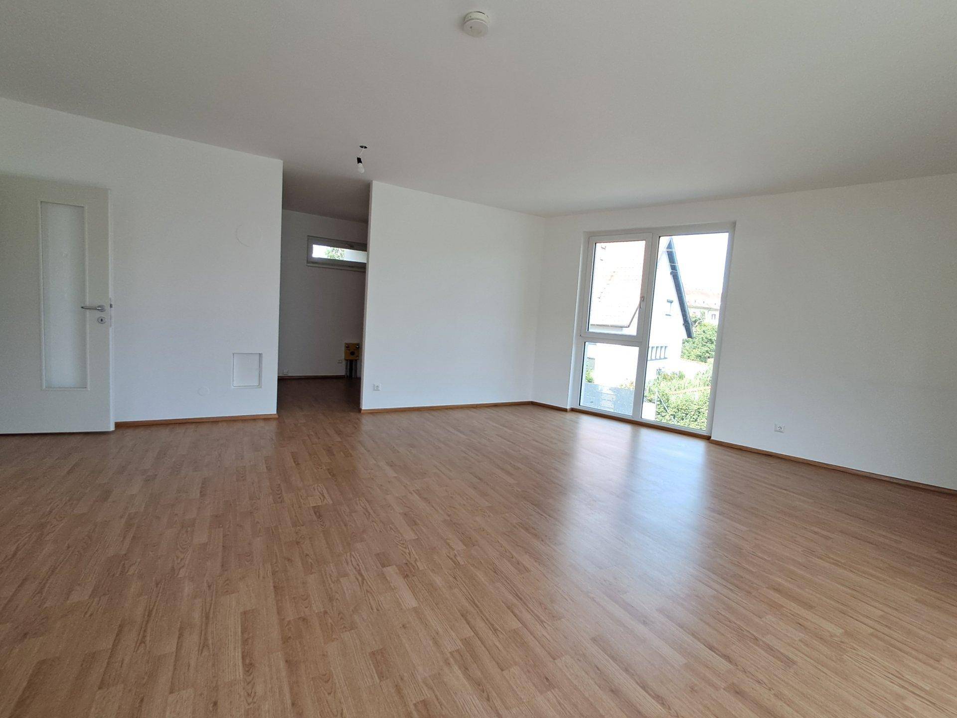 Geräumiges Wohnzimmer mit hellem Laminatboden und weiß gestrichenen Wänden, bereit zur Einrichtung.