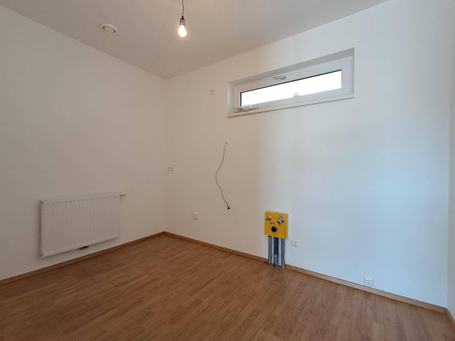 Leeres Zimmer mit Laminatboden, einem Fenster und Heizkörper, ideal als Schlaf- oder Arbeitszimmer.