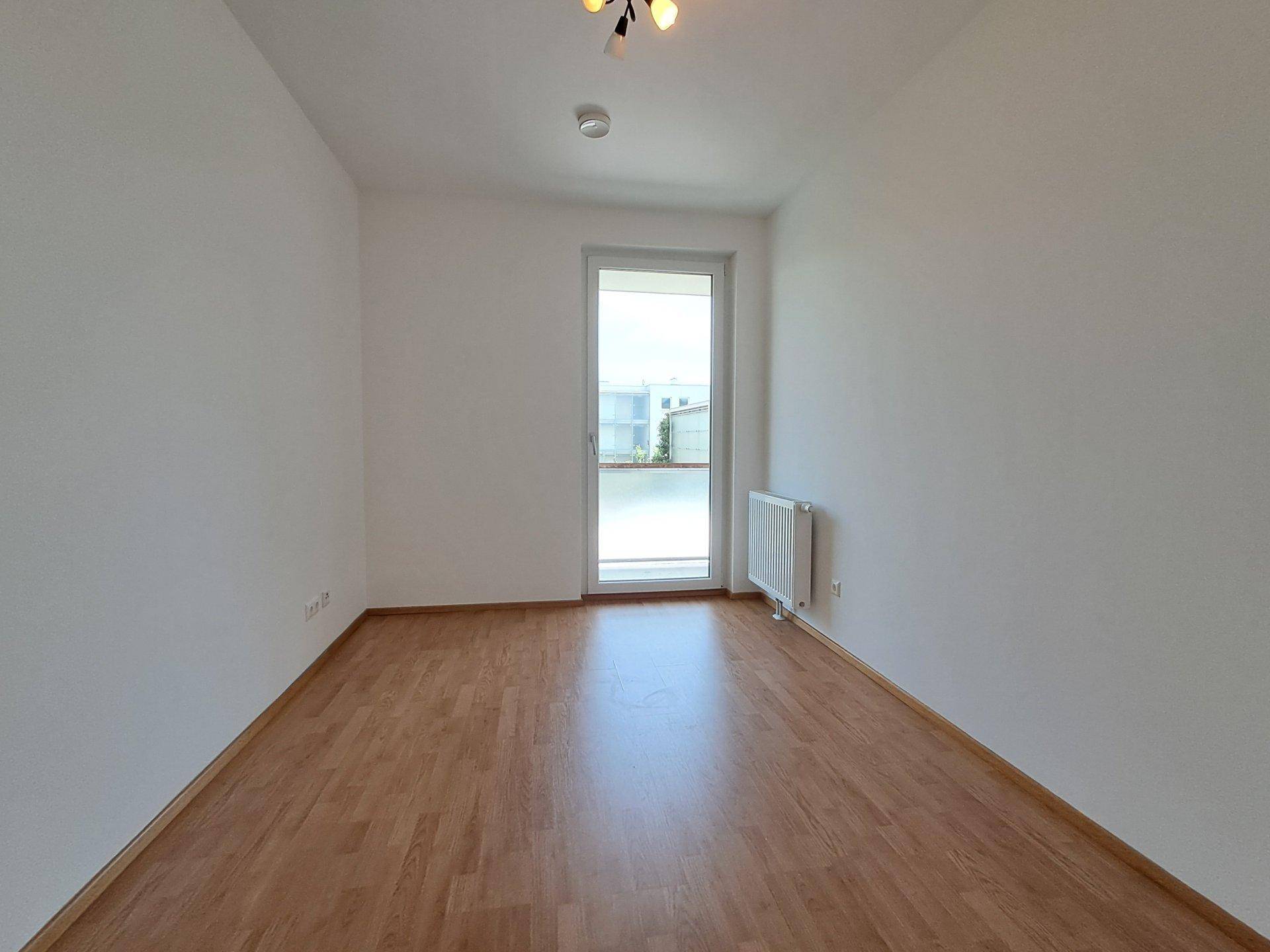 Leeres Zimmer mit Laminatboden und direktem Zugang zu einem Balkon, bietet viel Tageslicht.