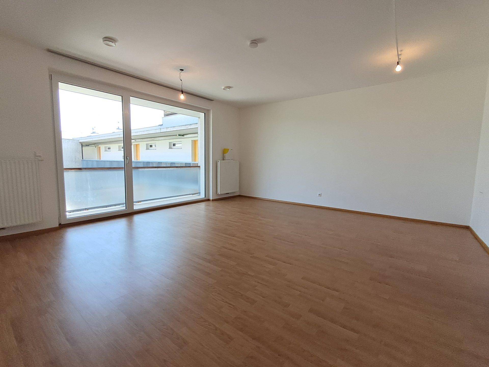 Großer, heller Wohnraum mit Laminatboden und bodentiefen Fenstern, die viel Licht hereinlassen.