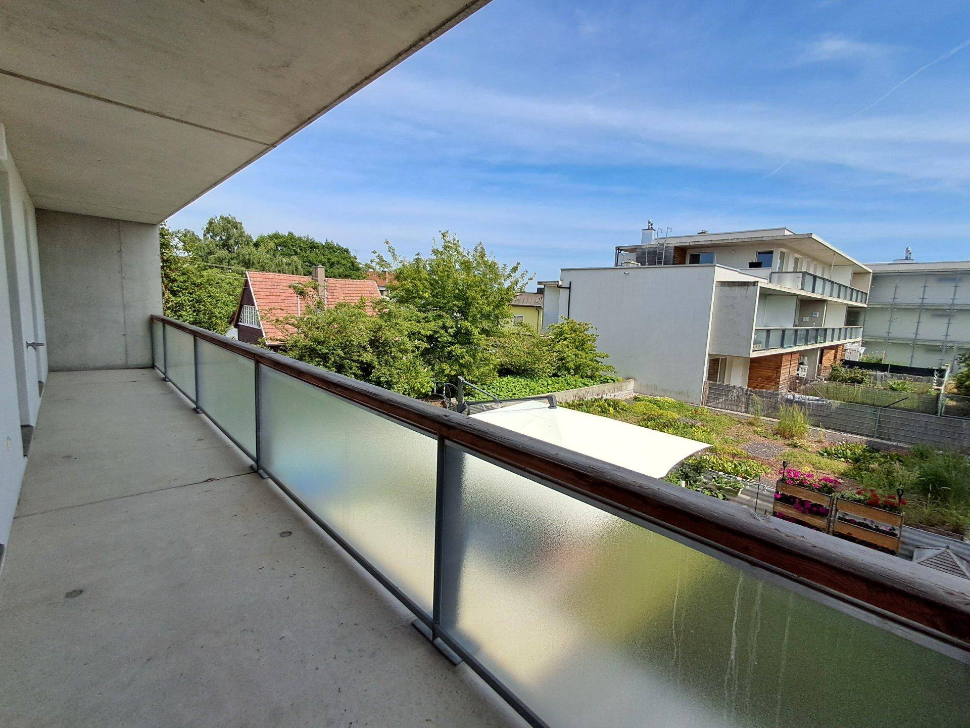 Balkon mit Milchglasgeländer und Blick auf den begrünten Innenhof sowie umliegende Gebäude.