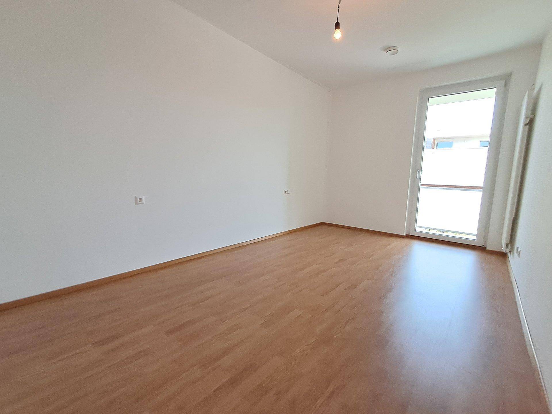 Leeres Zimmer mit Laminatboden und einem Fenster, das für natürliche Belichtung sorgt.