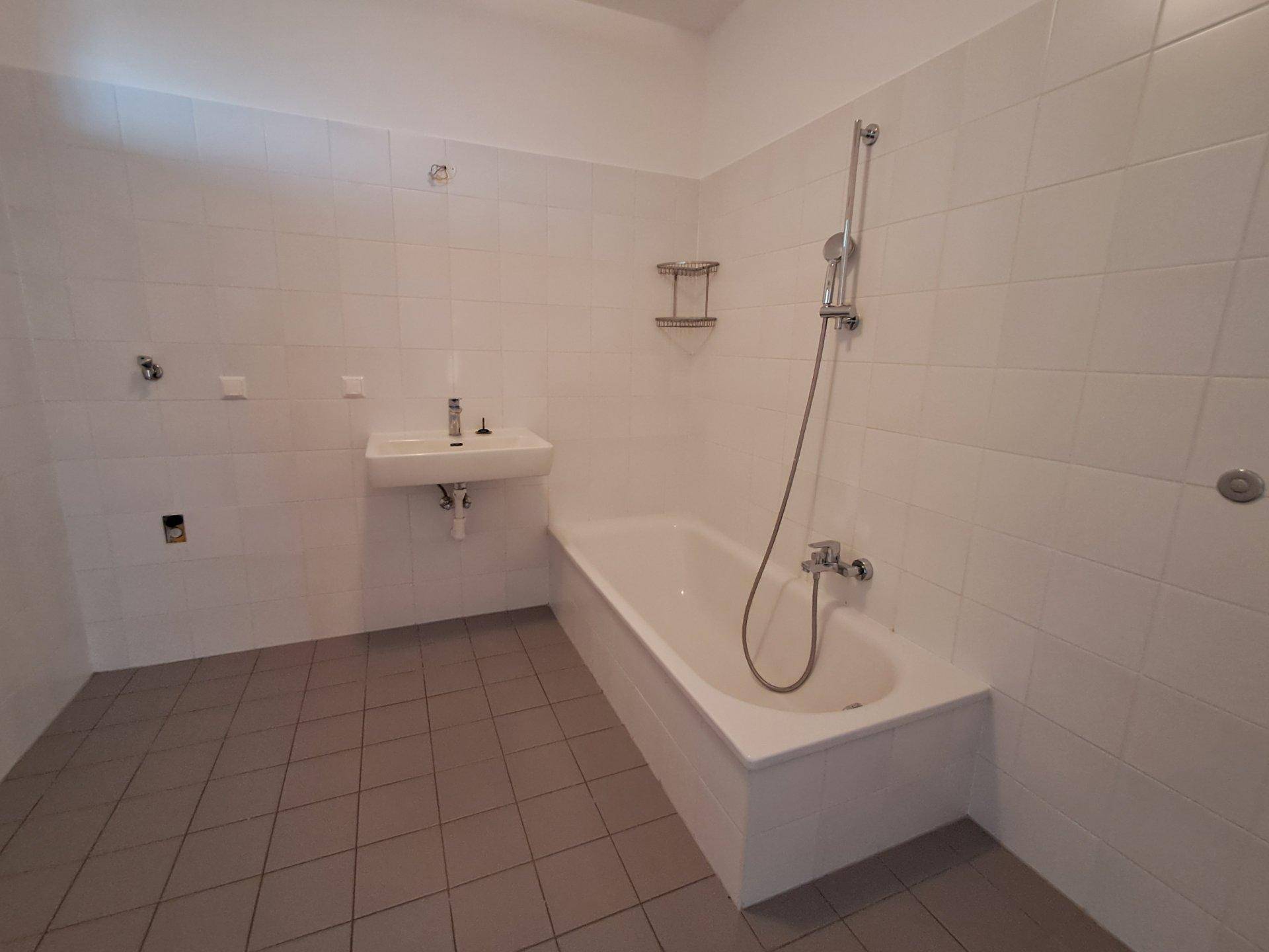 Funktionales Badezimmer mit Badewanne, Waschbecken und weißen Fliesen an den Wänden.