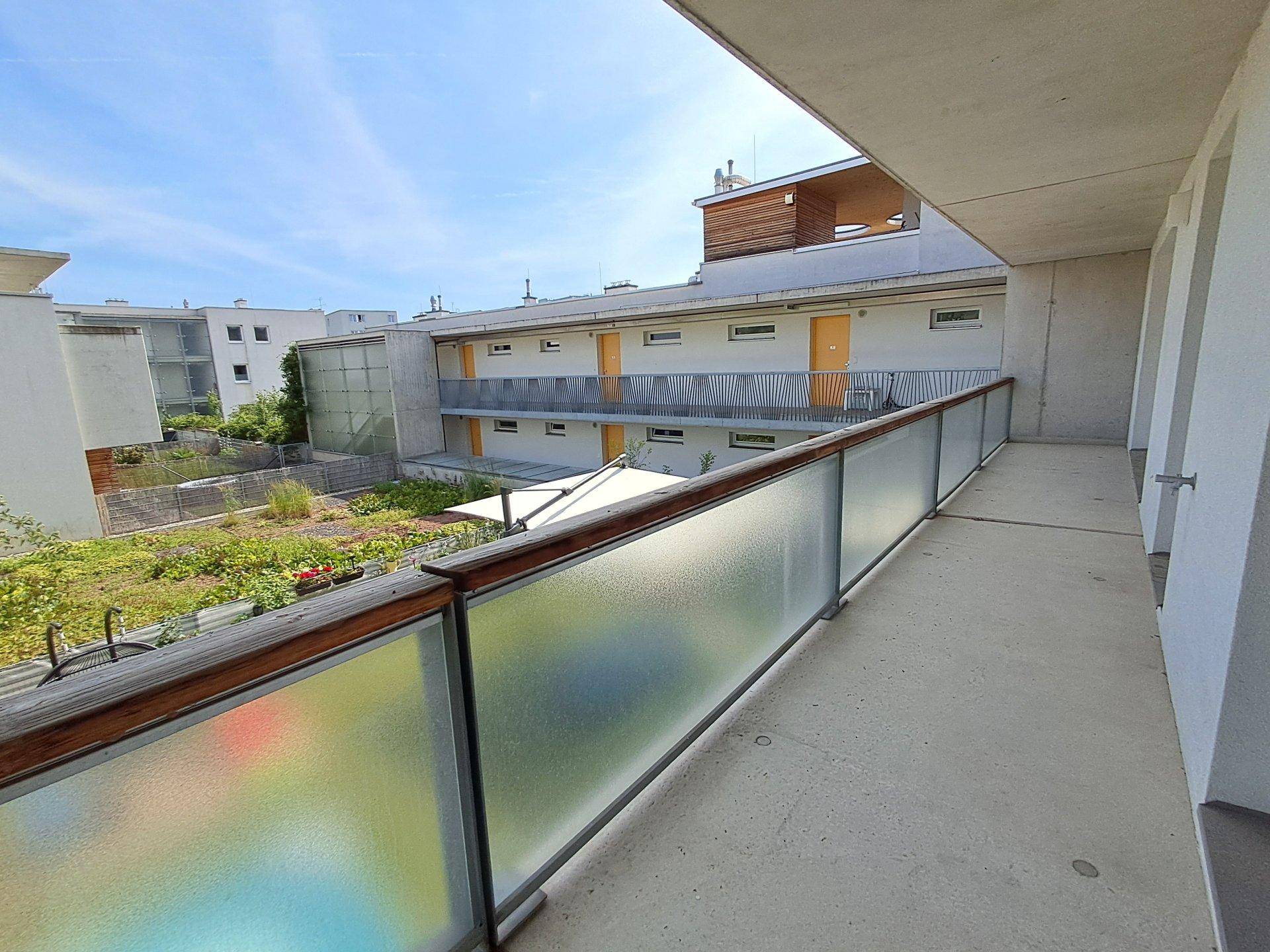 Langer Balkon oder Laubengang mit Blick auf den grünen Innenhof des Wohnkomplexes.