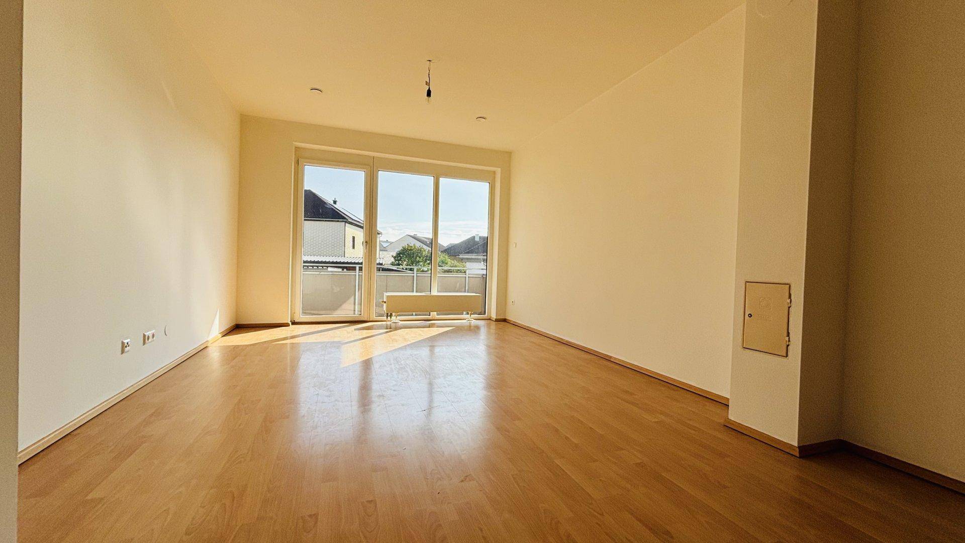 Helles, leeres Wohnzimmer mit Laminatboden und großem Fenster mit Zugang zum Balkon.