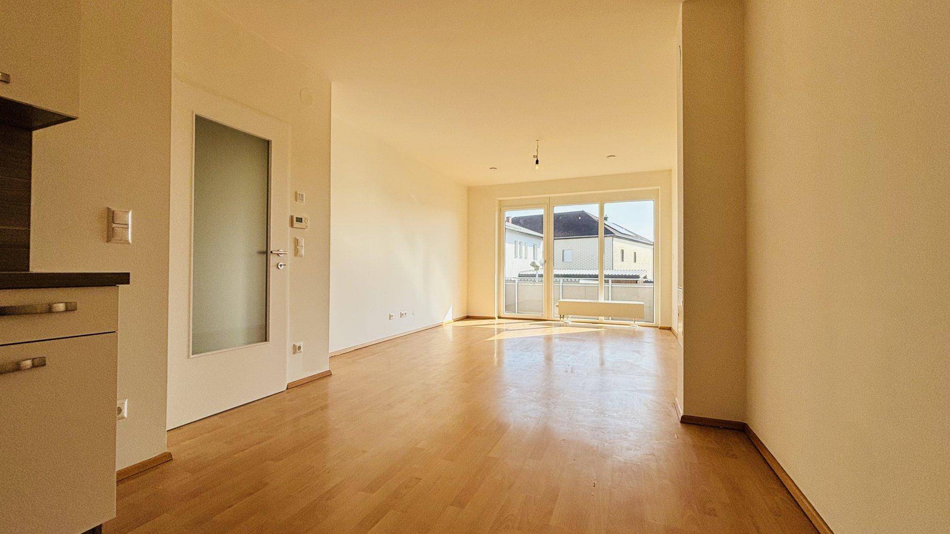 Geräumiges Wohnzimmer mit Laminatboden, viel Tageslicht und einer Tür zum Flur.