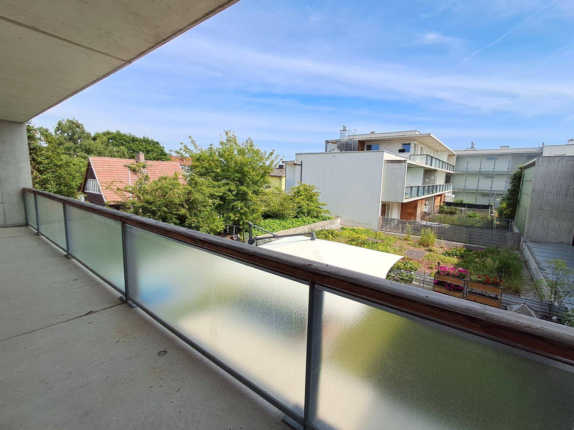 Balkon mit Milchglasgeländer und Blick auf den begrünten Innenhof sowie umliegende Gebäude.