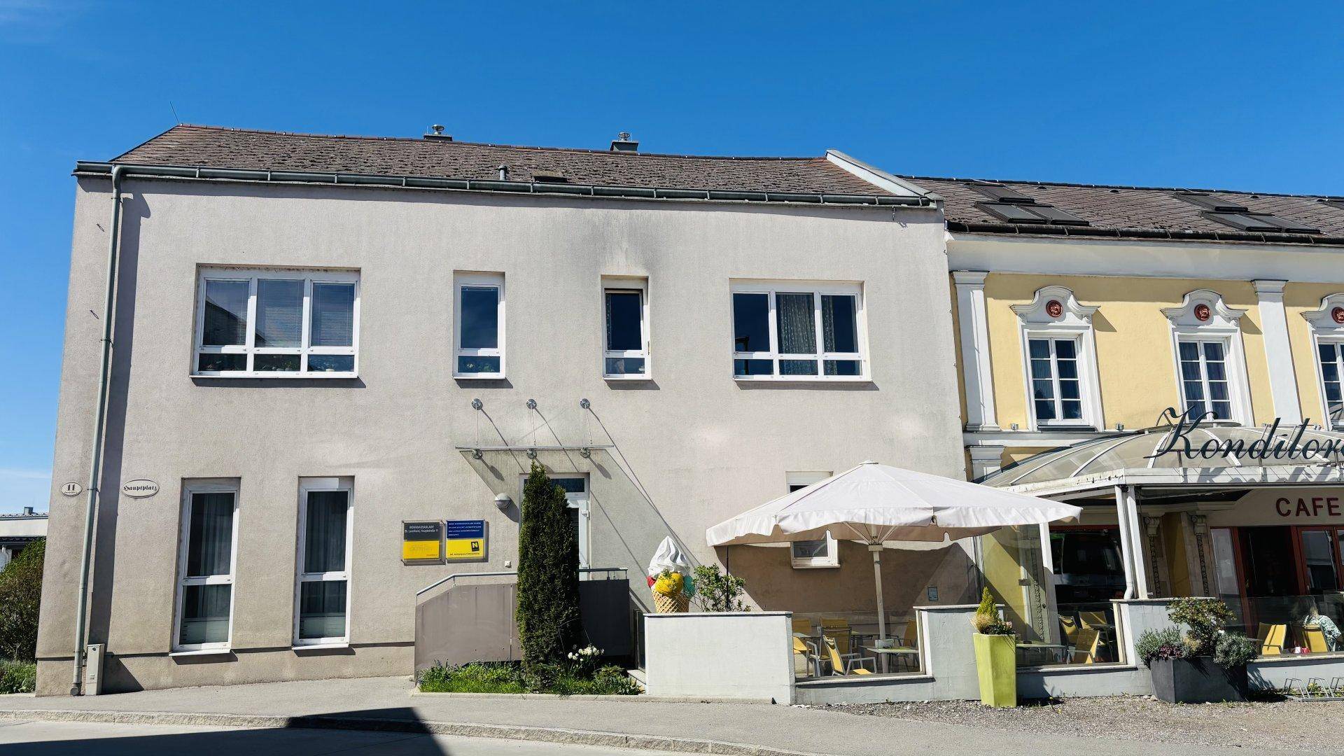 Fassade eines Wohngebäudes neben einem Café mit Sonnenschirm an einem sonnigen Tag.
