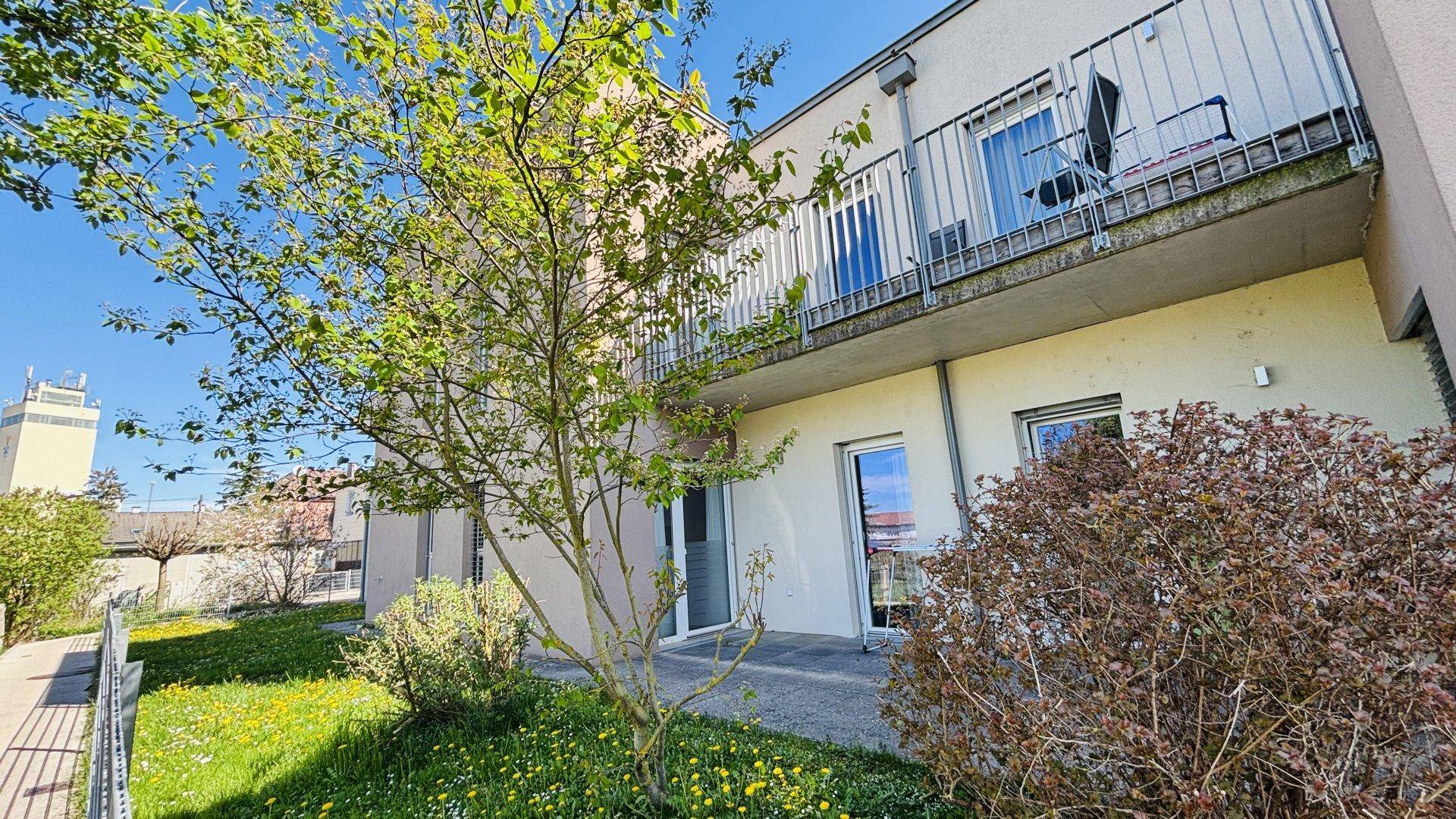 Grünfläche im Erdgeschoss mit Zugang zu einer Terrasse und einem darüberliegenden Balkon.