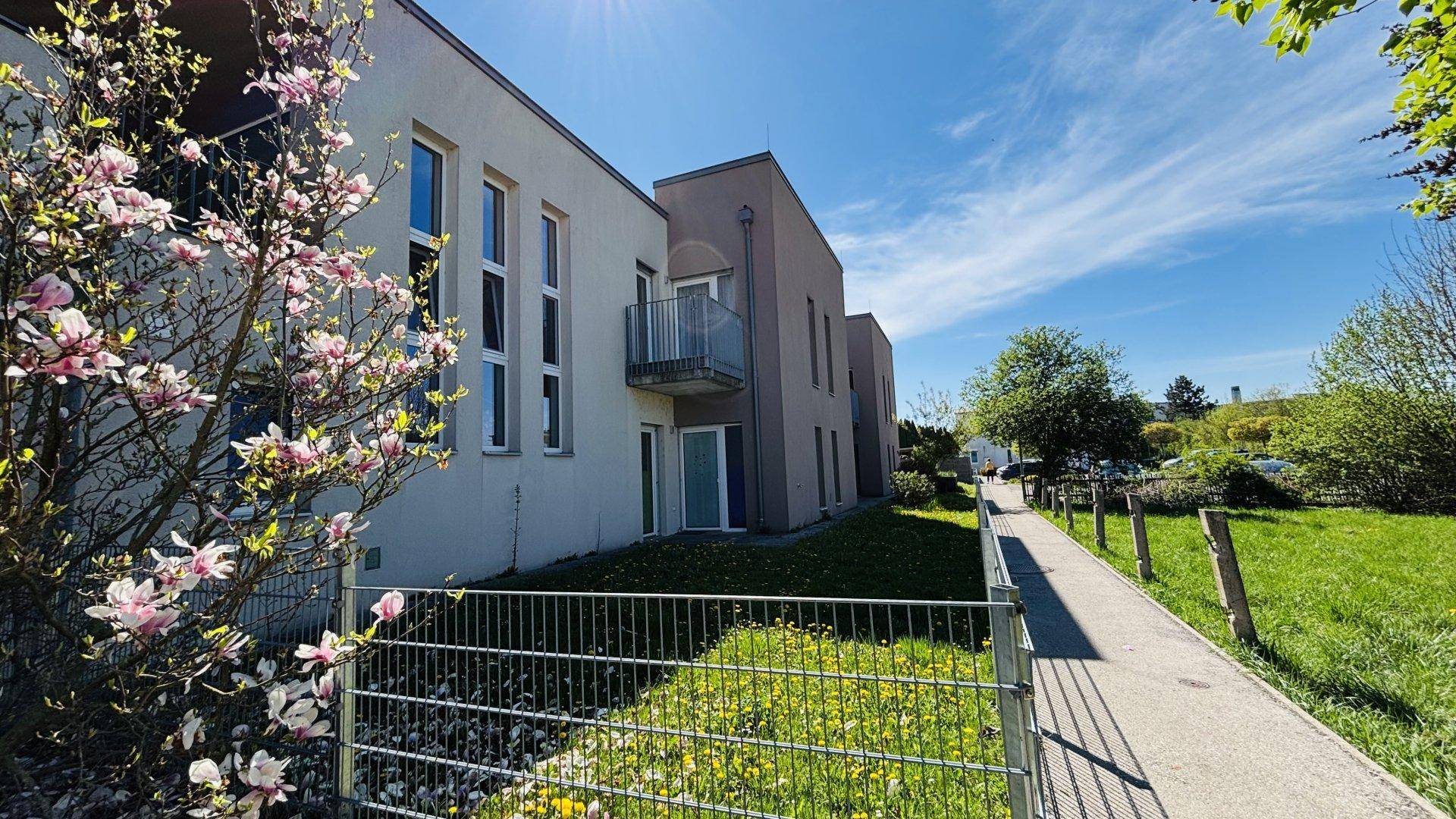 Seitenansicht eines modernen Wohngebäudes mit Balkonen und blühenden Bäumen im Frühling.