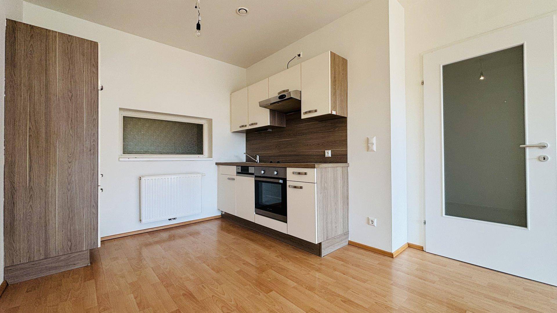 Kompakte Küchenzeile mit hellen Schränken, integriertem Backofen und Laminatboden.