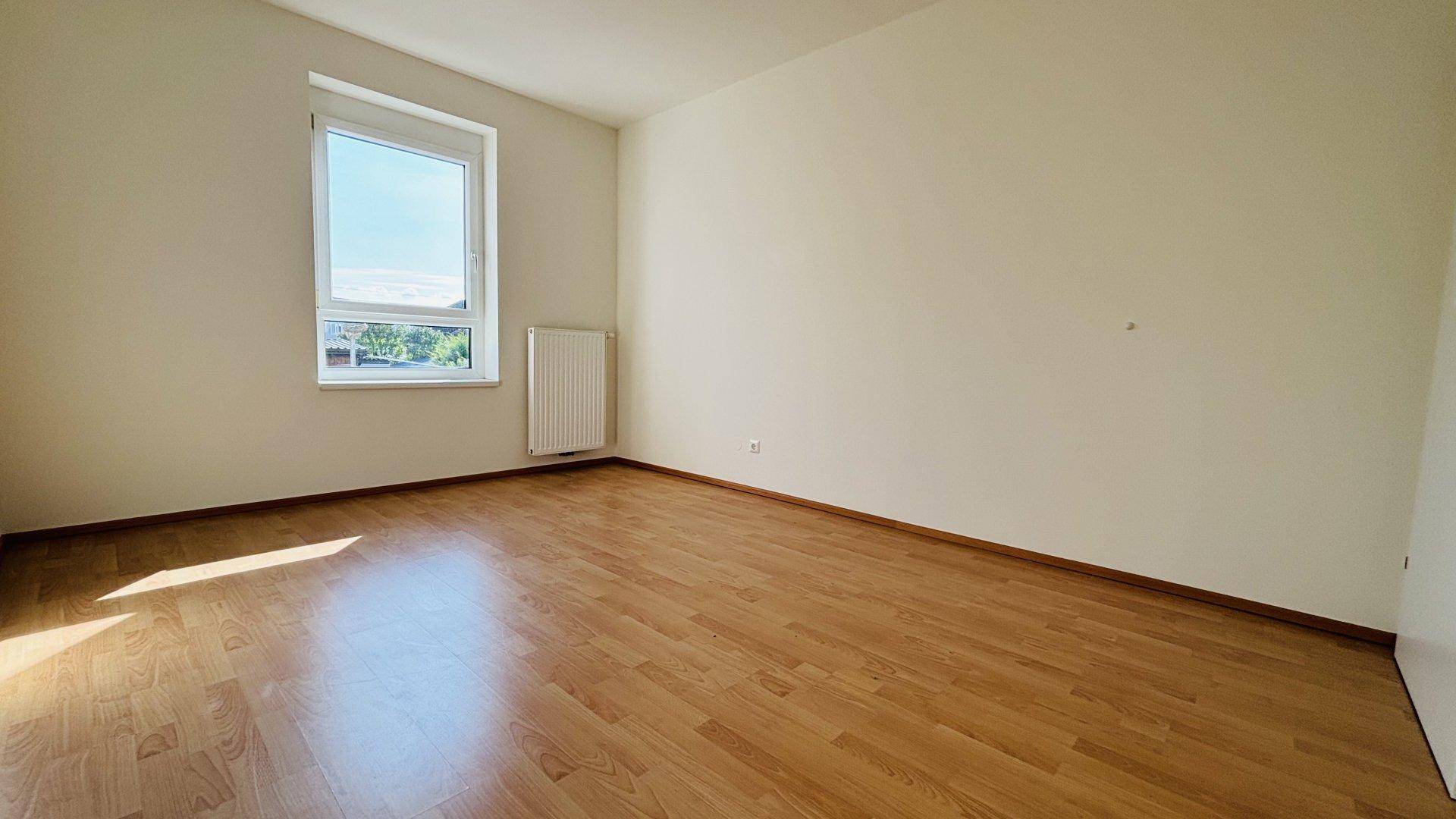 Helles Schlafzimmer mit Laminatboden und einem Fenster, das viel Tageslicht hereinlässt.
