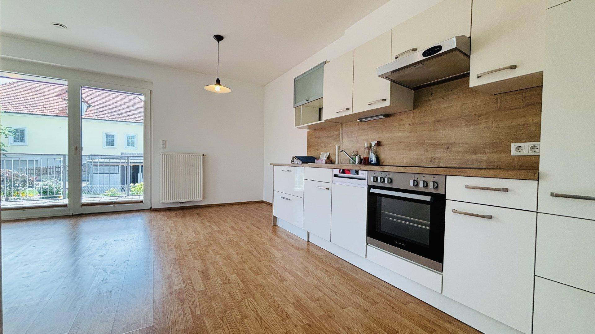 Offener Wohnbereich mit moderner Einbauküche, Laminatboden und Zugang zum Balkon.