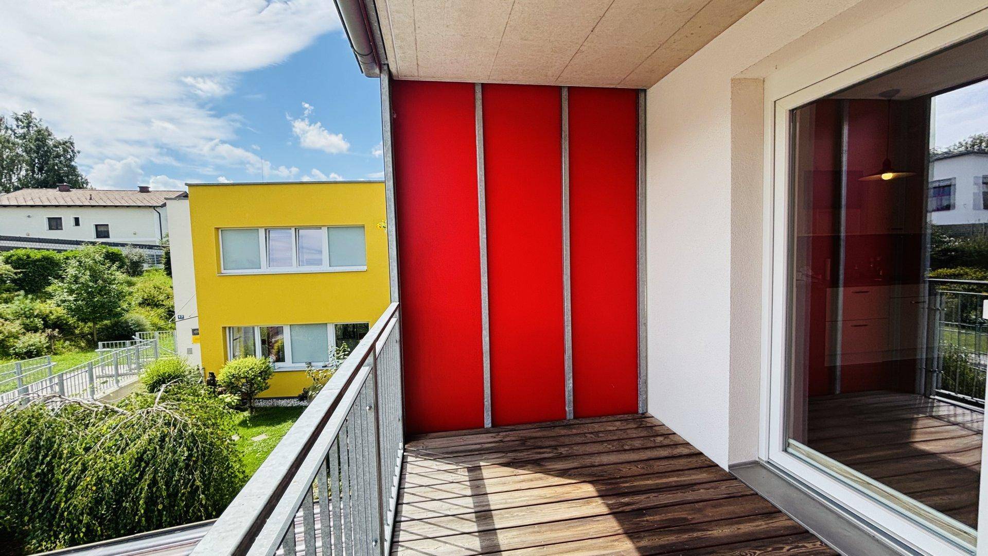 Heller Balkon mit Holzboden und Blick auf die farbige Fassade des Gebäudes.