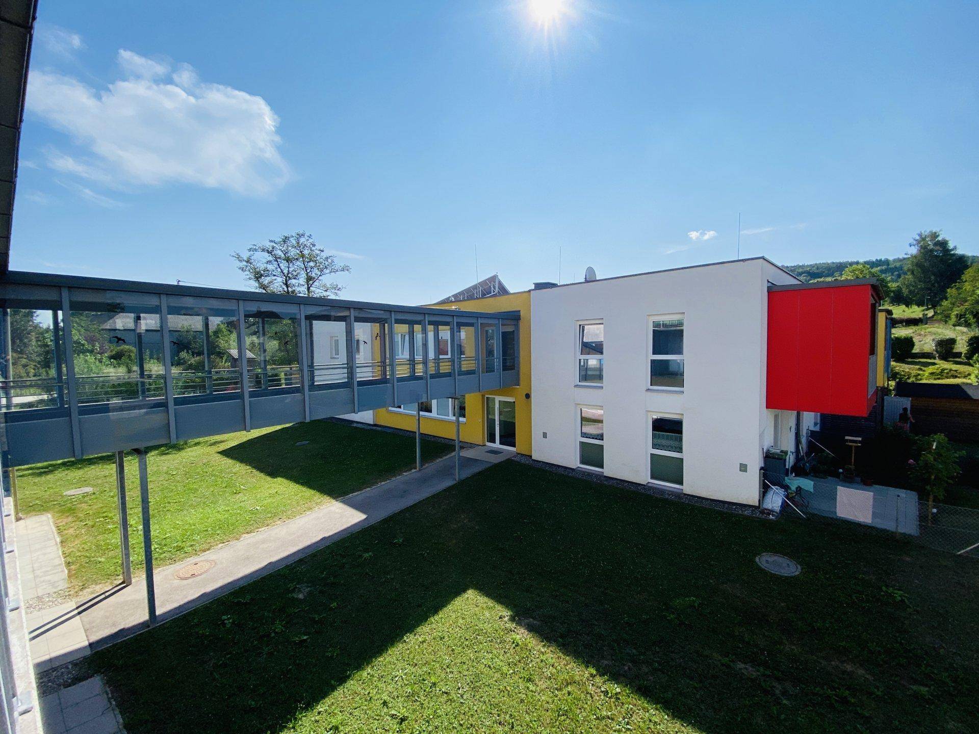 Moderne Wohnanlage mit Glassteg und gepflegter Rasenfläche unter strahlend blauem Himmel.
