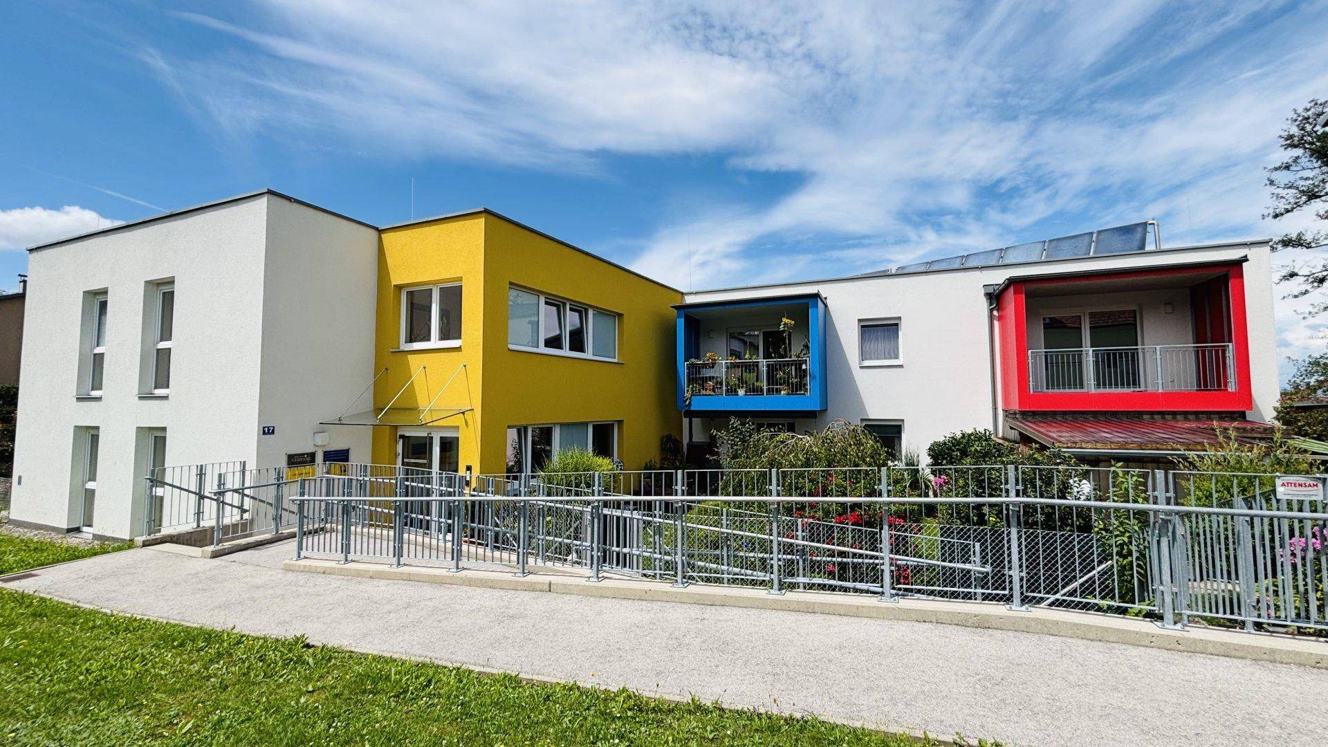 Ansicht der modernen Wohnanlage mit barrierefreier Rampe und farbigen Balkonen.