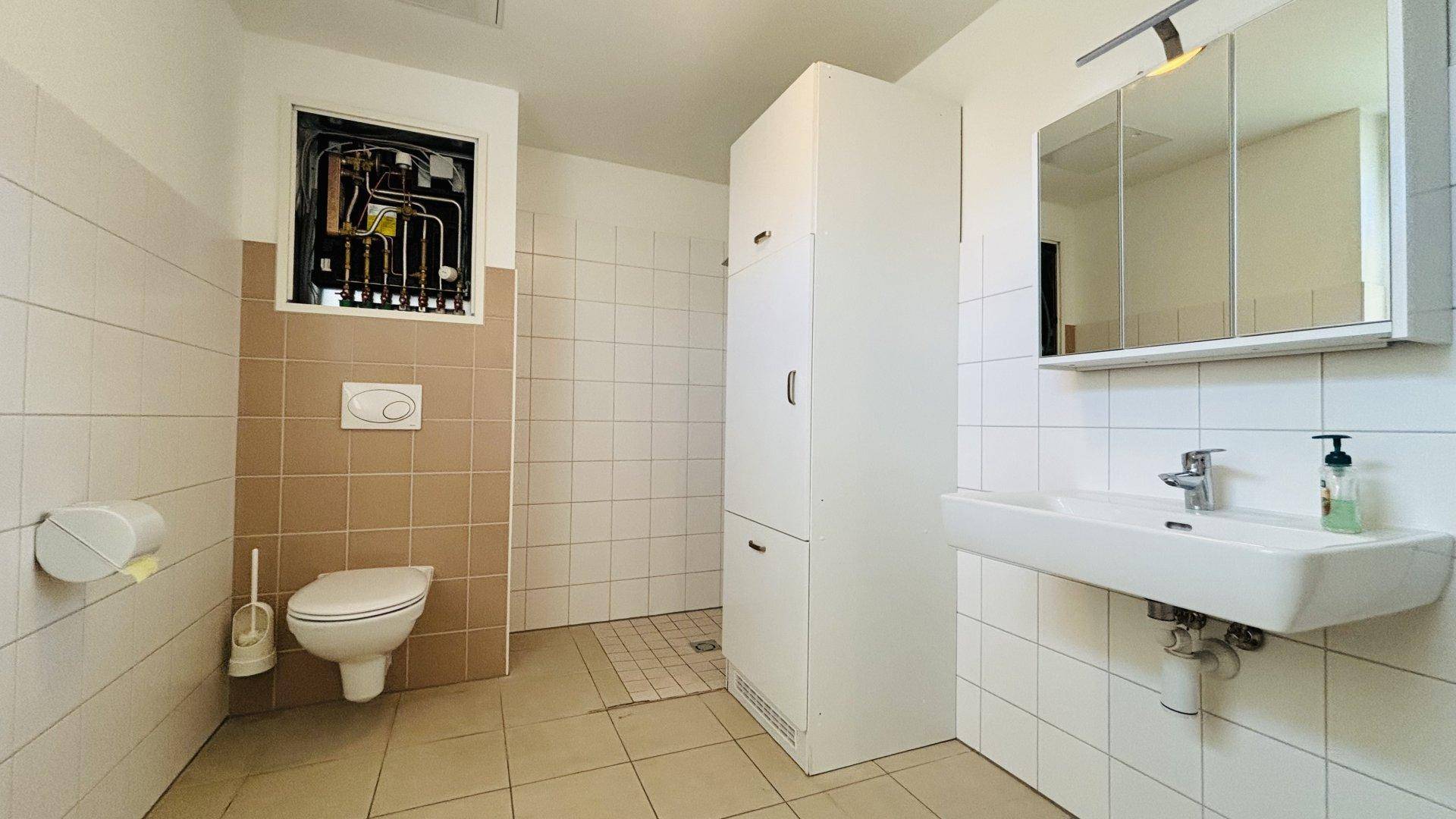 Modernes Badezimmer mit Fliesenboden, Dusche, WC und Waschbecken mit Spiegelschrank.